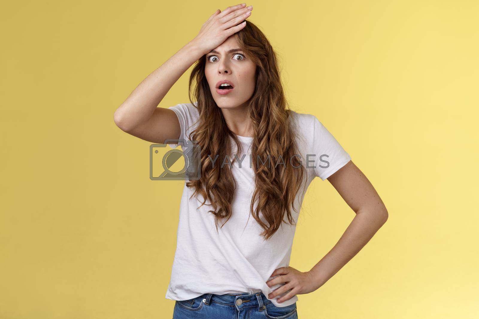 Royalty free image of Troubled distressed bothered shocked curly-haired girl realising make stupid mistake punch forehead gasping cringe grimace bothered facepalming upset remember important task by Benzoix