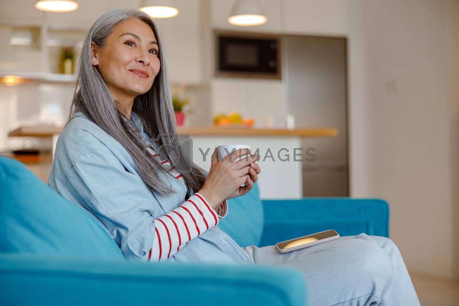 Royalty free image of Smiling woman with cup of coffee sitting on couch at home by Yaroslav_astakhov