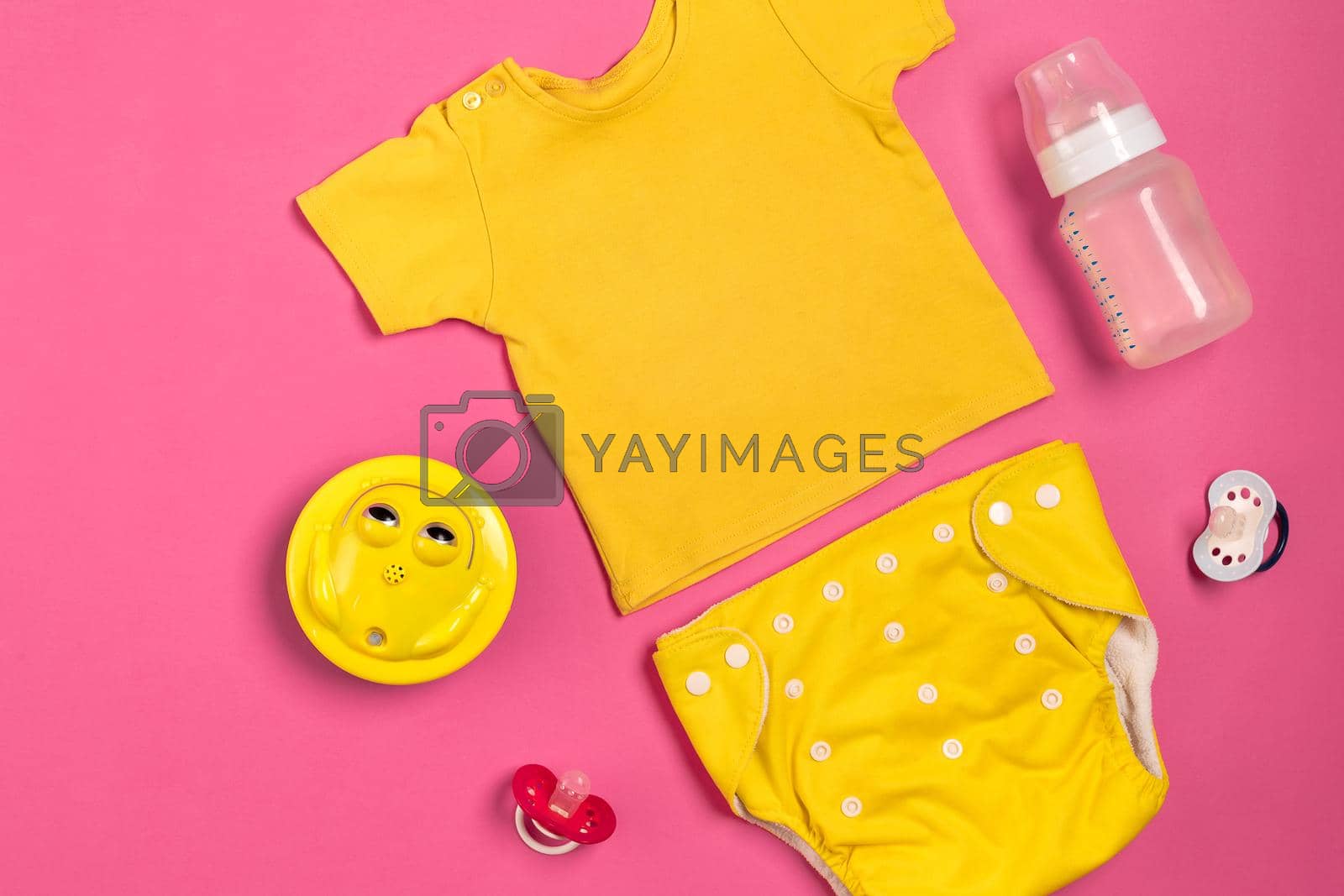 Yellow children's costume, bottle and orthodontic pacifier on a pink background. Top view. Copy space. Flat lay. Still life
