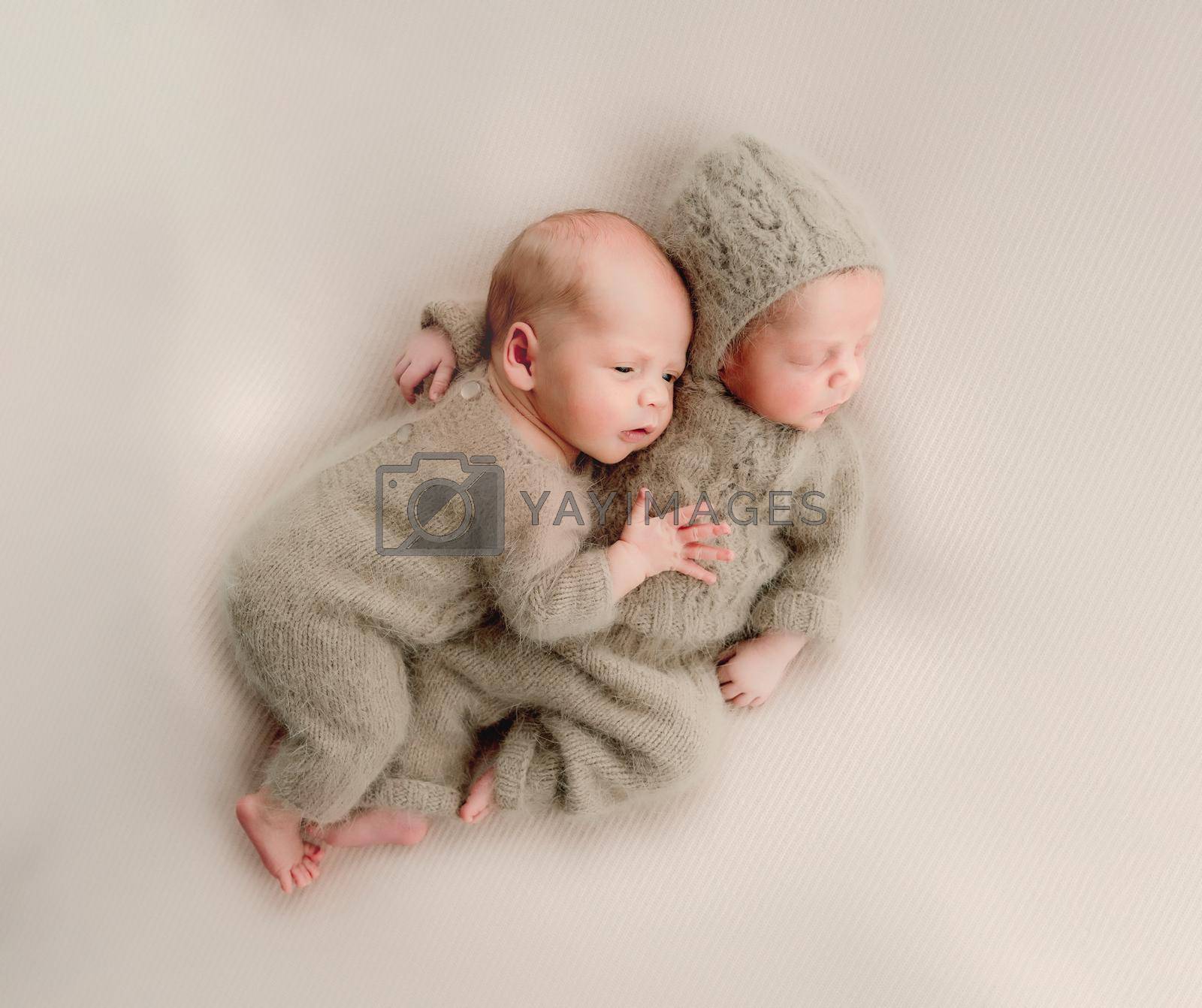 Twins newborn babies sleeping wearing knitted costumes and hugging each other studio portrait. Siblings brothers infant children napping together