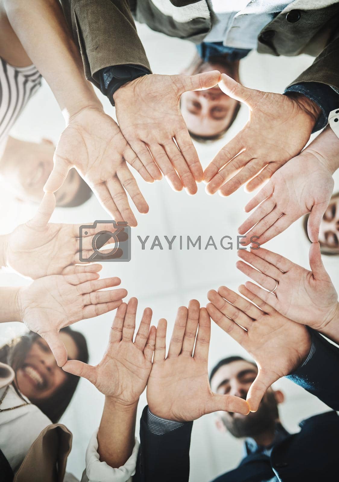Royalty free image of Together their brains work as one. Low angle shot of a group of cheerful businesspeople forming a huddle with their hands and looking down inside of the office. by YuriArcurs