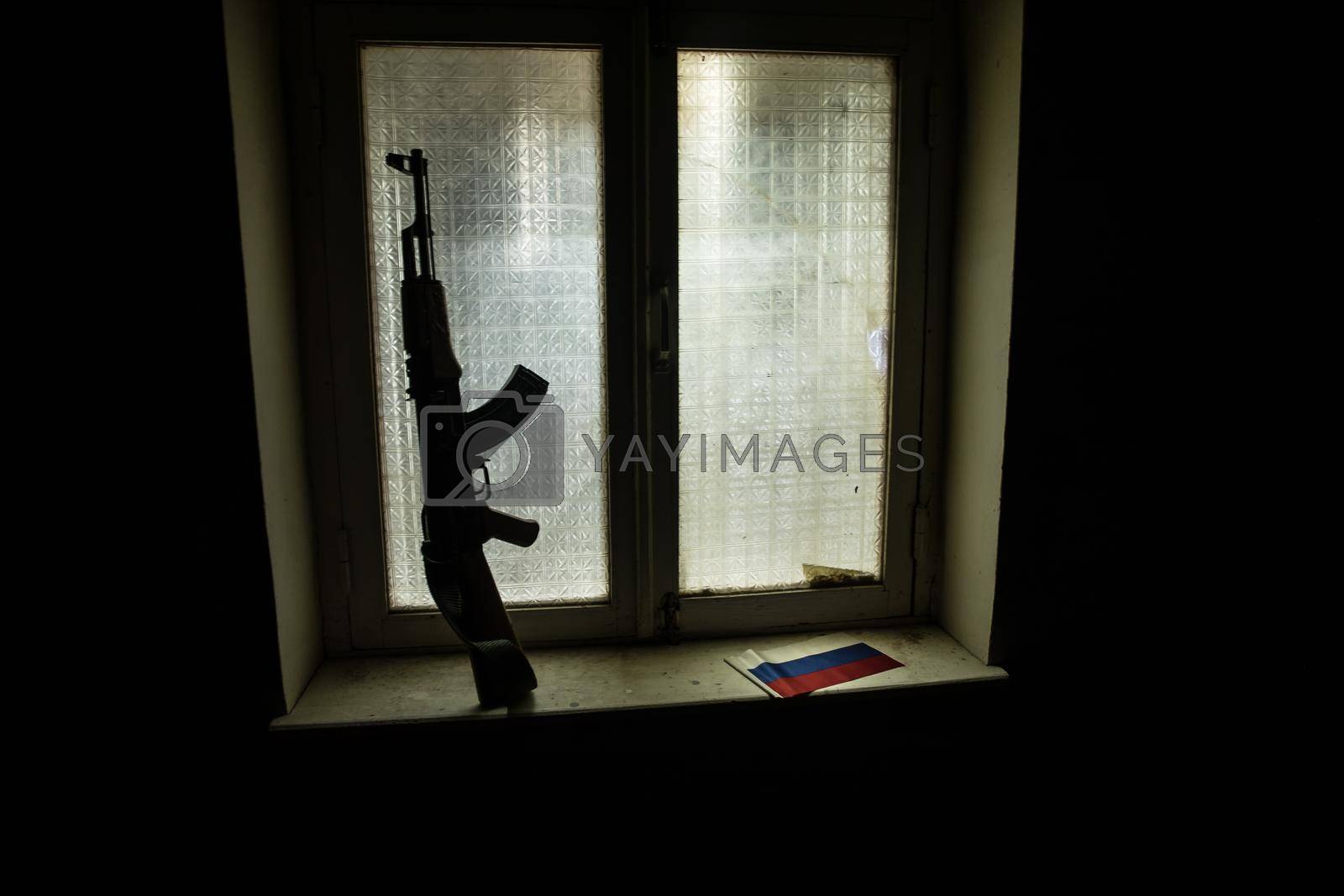 Conceptual photo of war between Russia and Ukraine. Russian flag and soviet gun on windowsill at night. Old creepy room with window. Explosion outside.