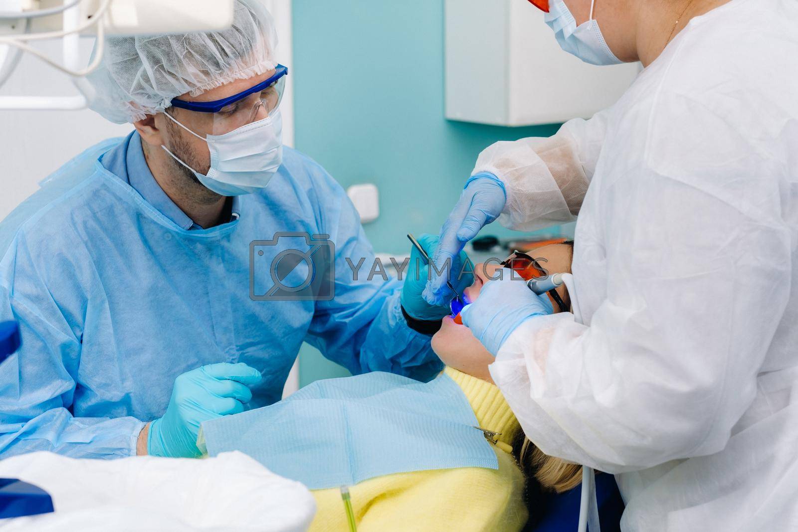 A female patient in dental glasses treats teeth at the dentist with ultraviolet light. dental fillings.