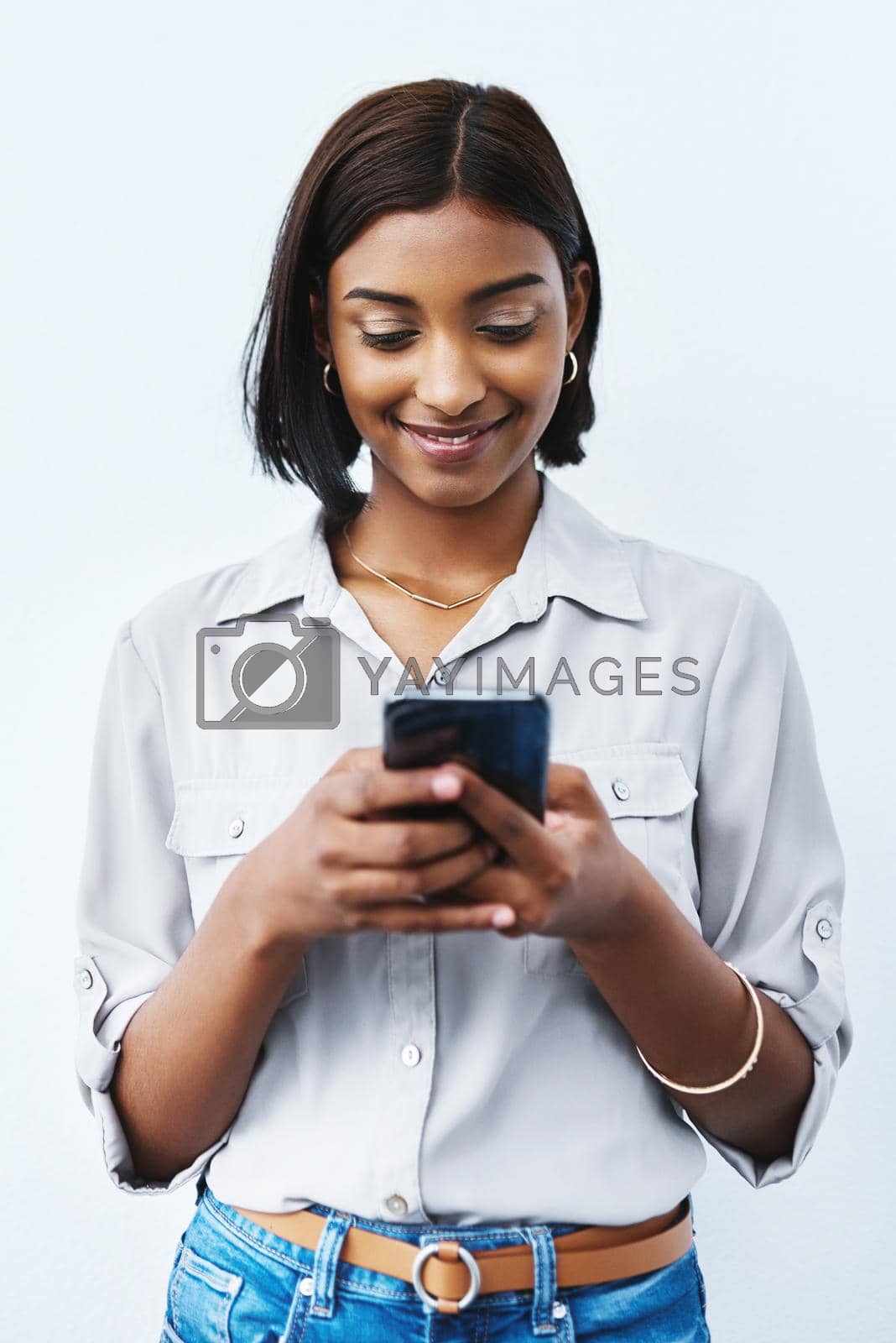 Royalty free image of When you get that message that brightens up your day. Studio shot of a young creative businesswoman using her cellphone and posing against a grey background. by YuriArcurs