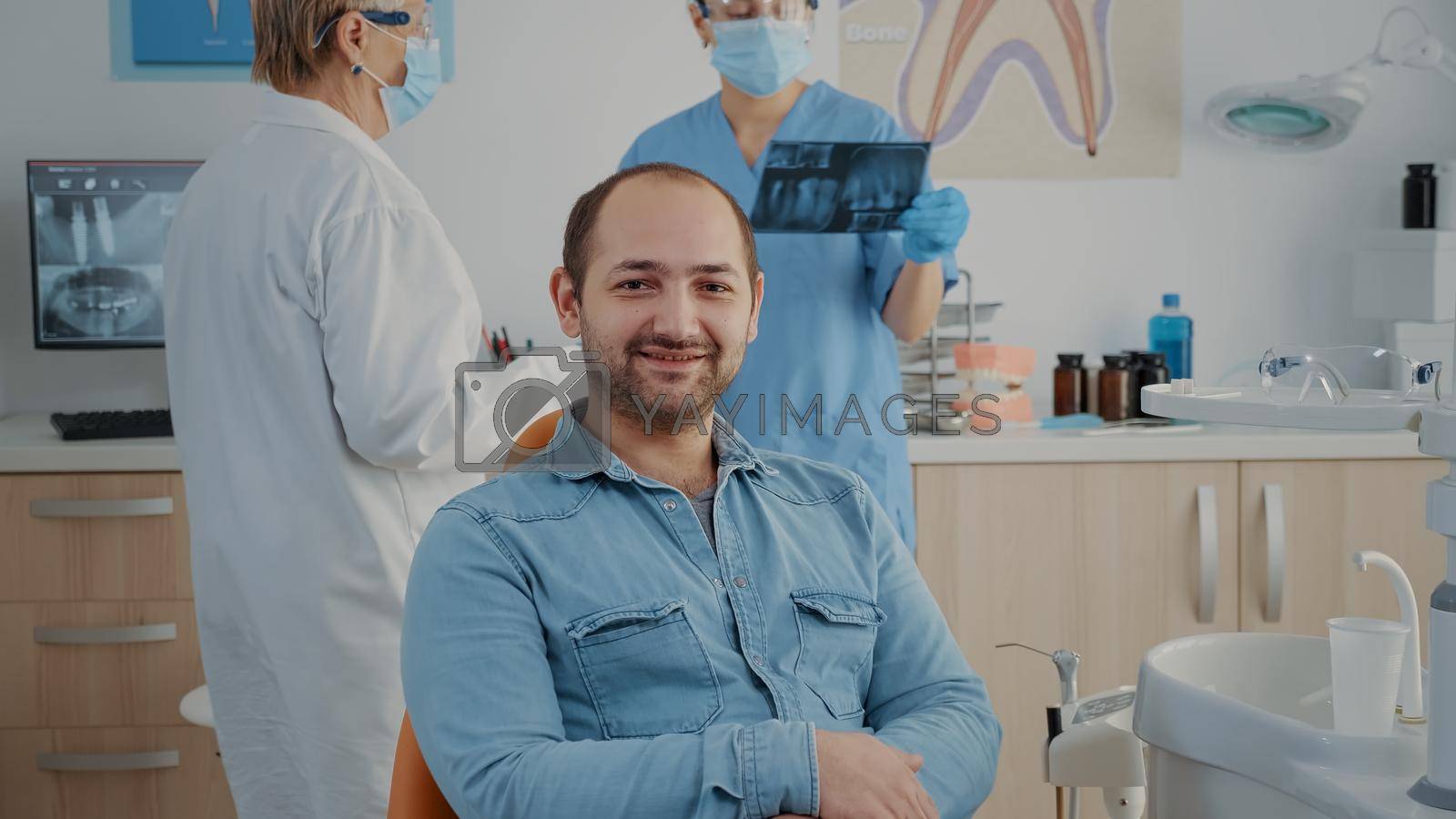 Portrait of patient sitting in dental chair at oral care clinic, looking at camera and smiling. Caucasian man having stomatological appointment with dentistry specialist in cabinet.