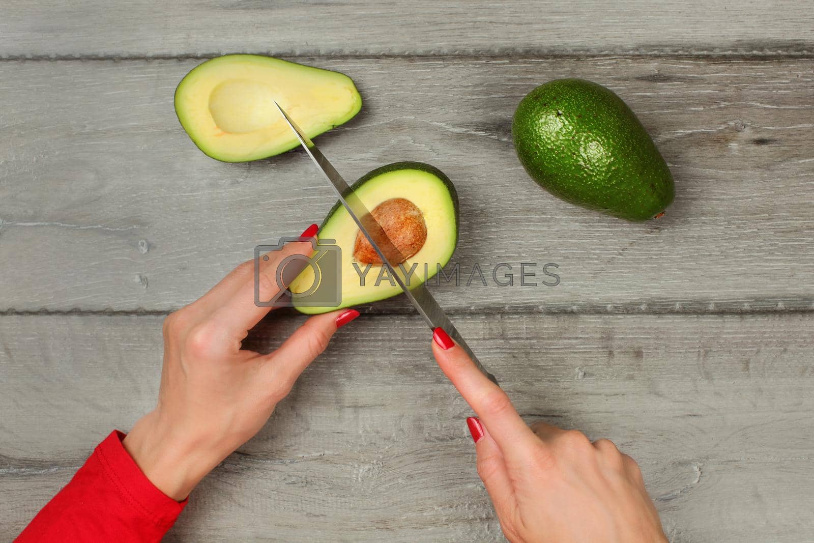Royalty free image of Tabletop view - woman hands holding chef knife, removing seed from avocado cut in half. by Ivanko