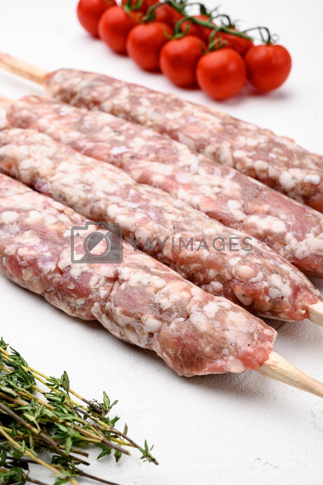 Royalty free image of Minced and shaped lamb mutton kebabs, with grill ingredients, on white stone table background by Ilianesolenyi