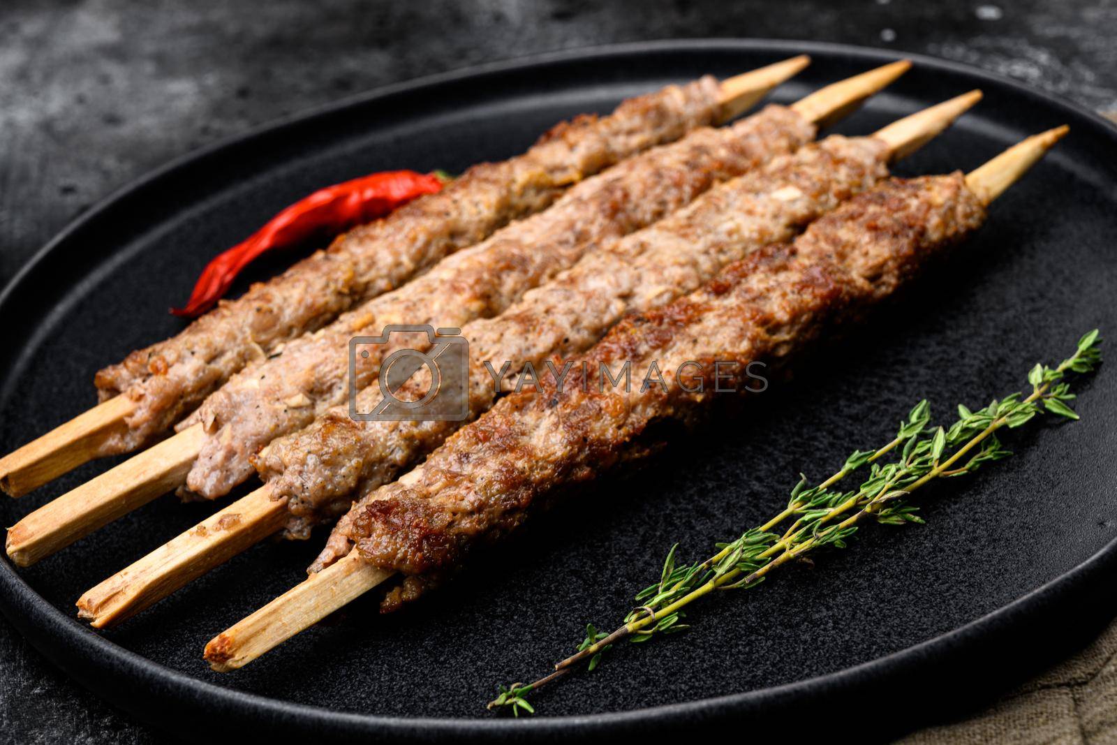 Royalty free image of Minced and shaped lamb mutton kebabs, on plate, on black dark stone table background by Ilianesolenyi