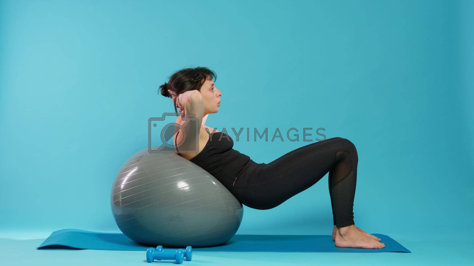 Athletic person doing physical effort on fitness toning ball, training body muscles. Fit woman using sport equipment to do gymnastics exercise and endurance activity over background.