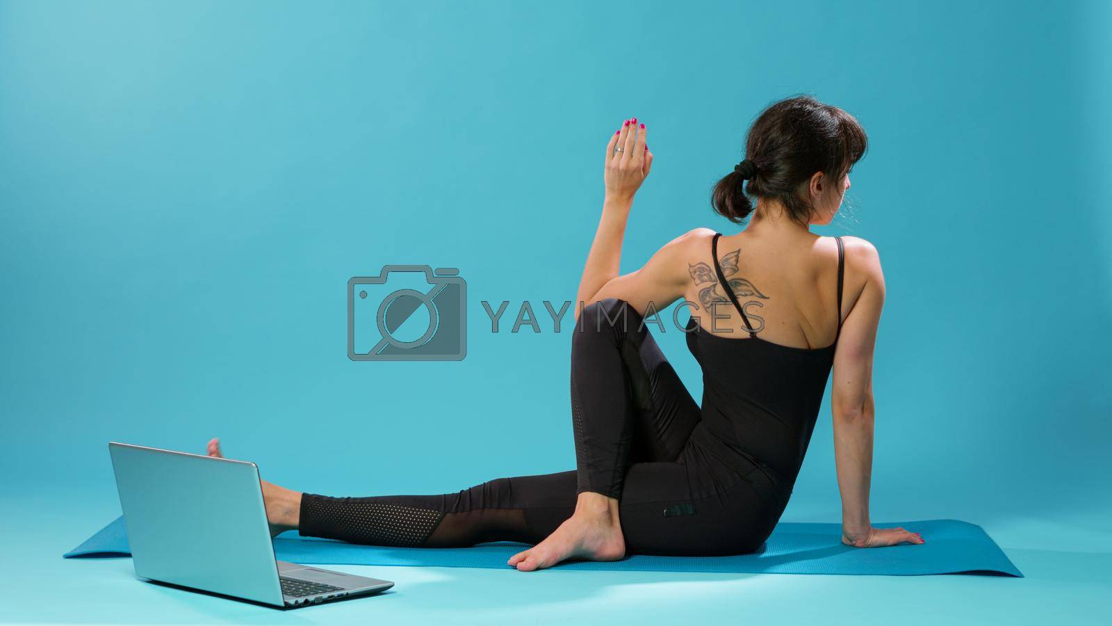 Active person stretching body muscles after fitness training, looking at online pilates video on laptop. Woman using wellness lesson to stretch arms and legs, recovering after workout activity.