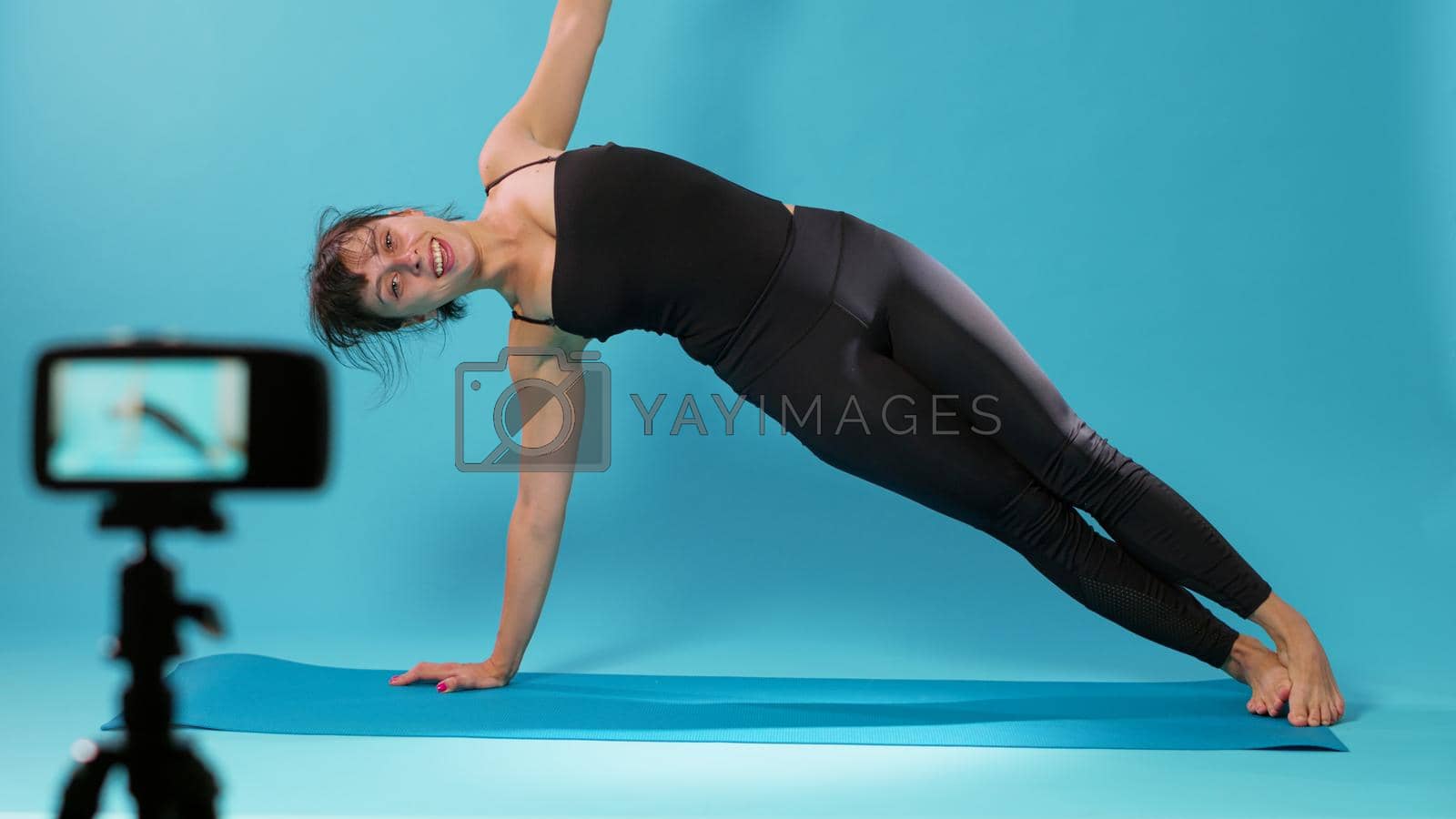 Yoga instructor filming stretching exercise on camera in studio, showing relaxing moves after intense body workout. Woman recording stretch activity on video for online training class.
