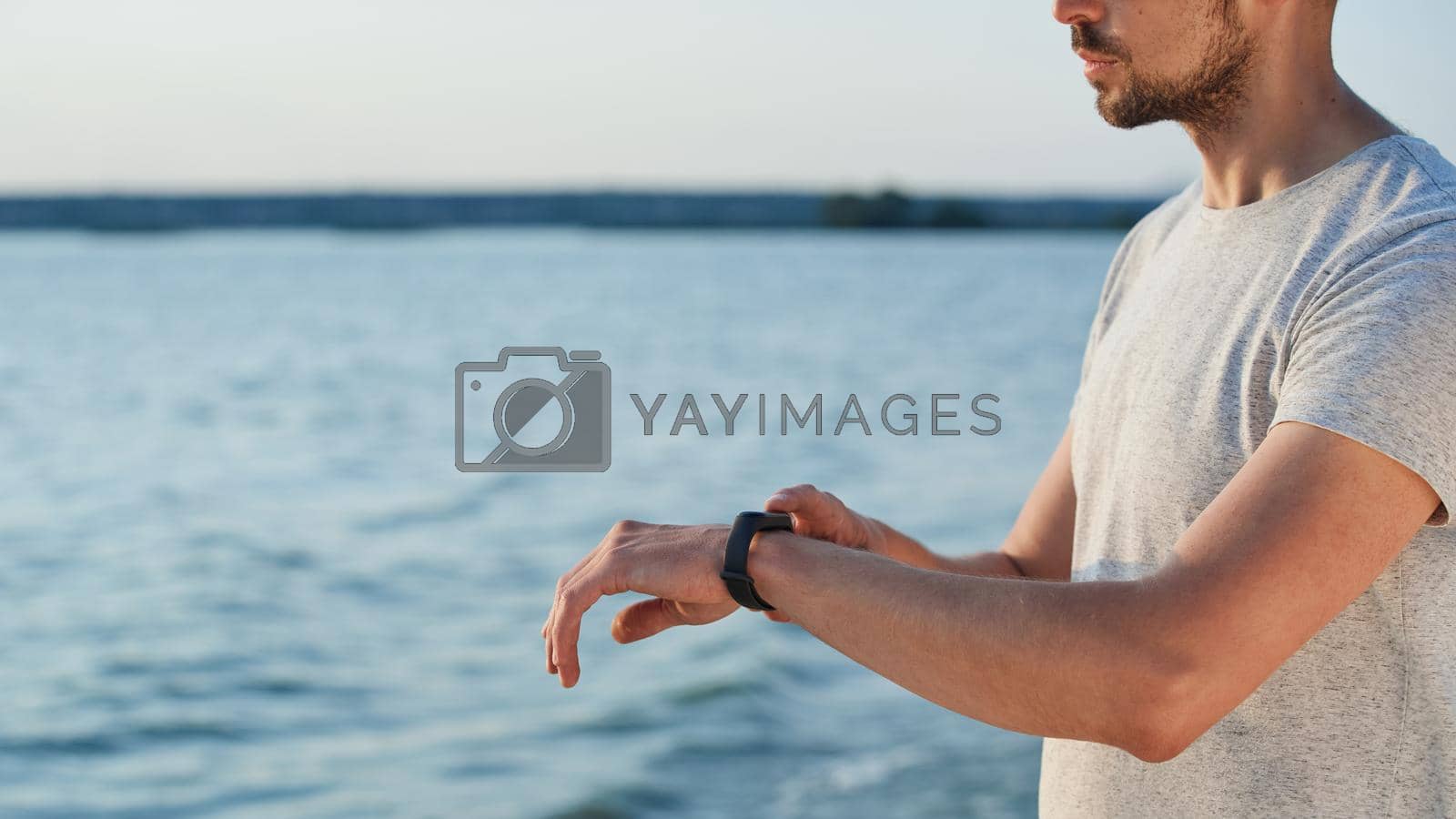 sporty man with a smart fitness watch standing on the seashore close-up. .