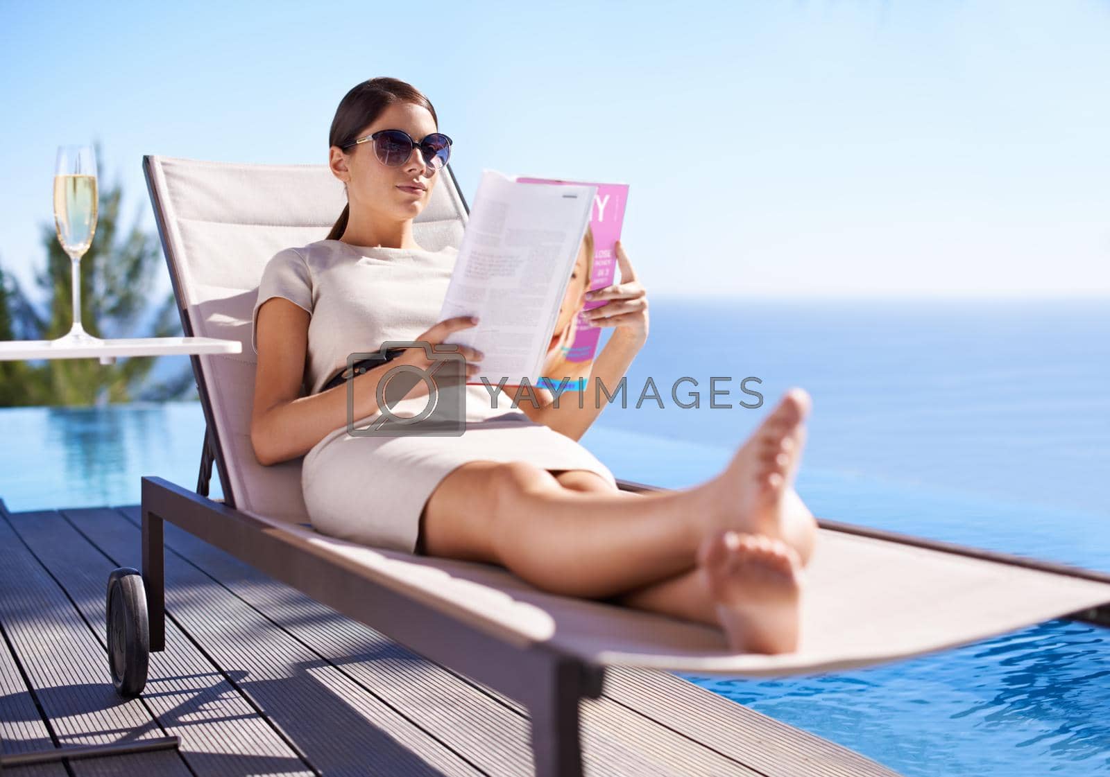 Royalty free image of Enjoying her vacation. An attractive young woman reading a magazine while lying on a deck chair. by YuriArcurs