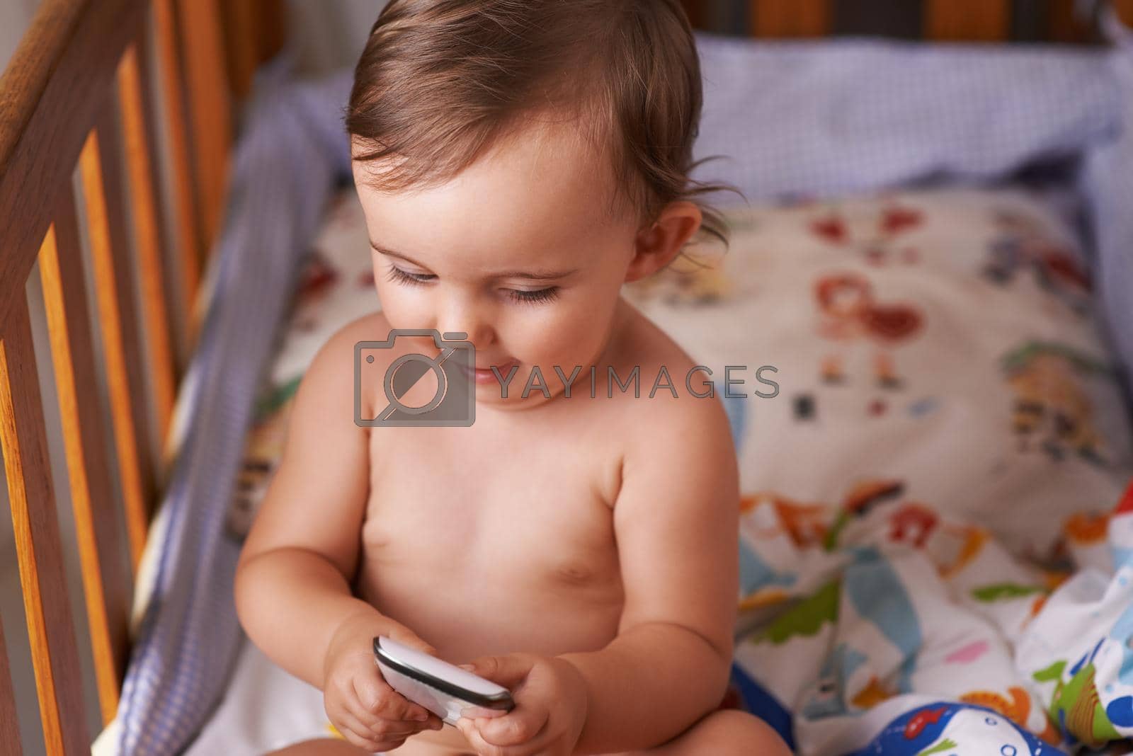 A little girl sitting in her crib playing with her cellphone.