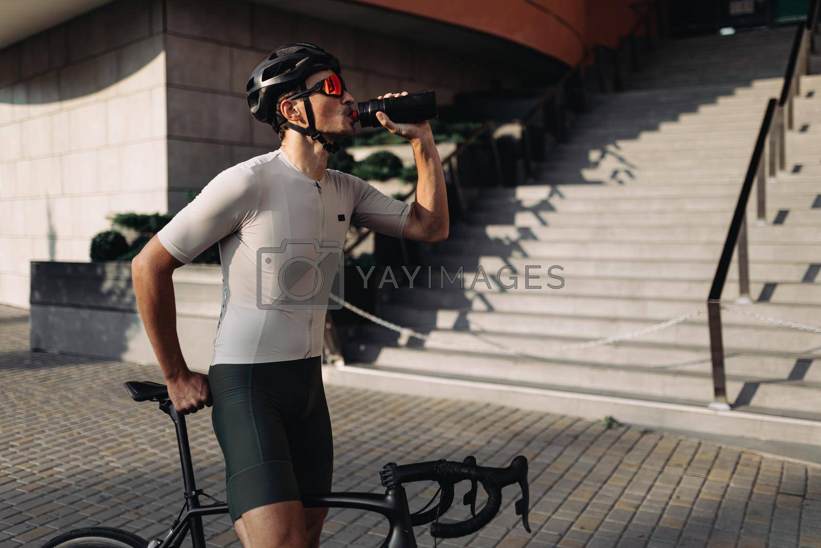 Royalty free image of Cyclist and helmet and glasses drinking water outdoors by Tymoshchuk