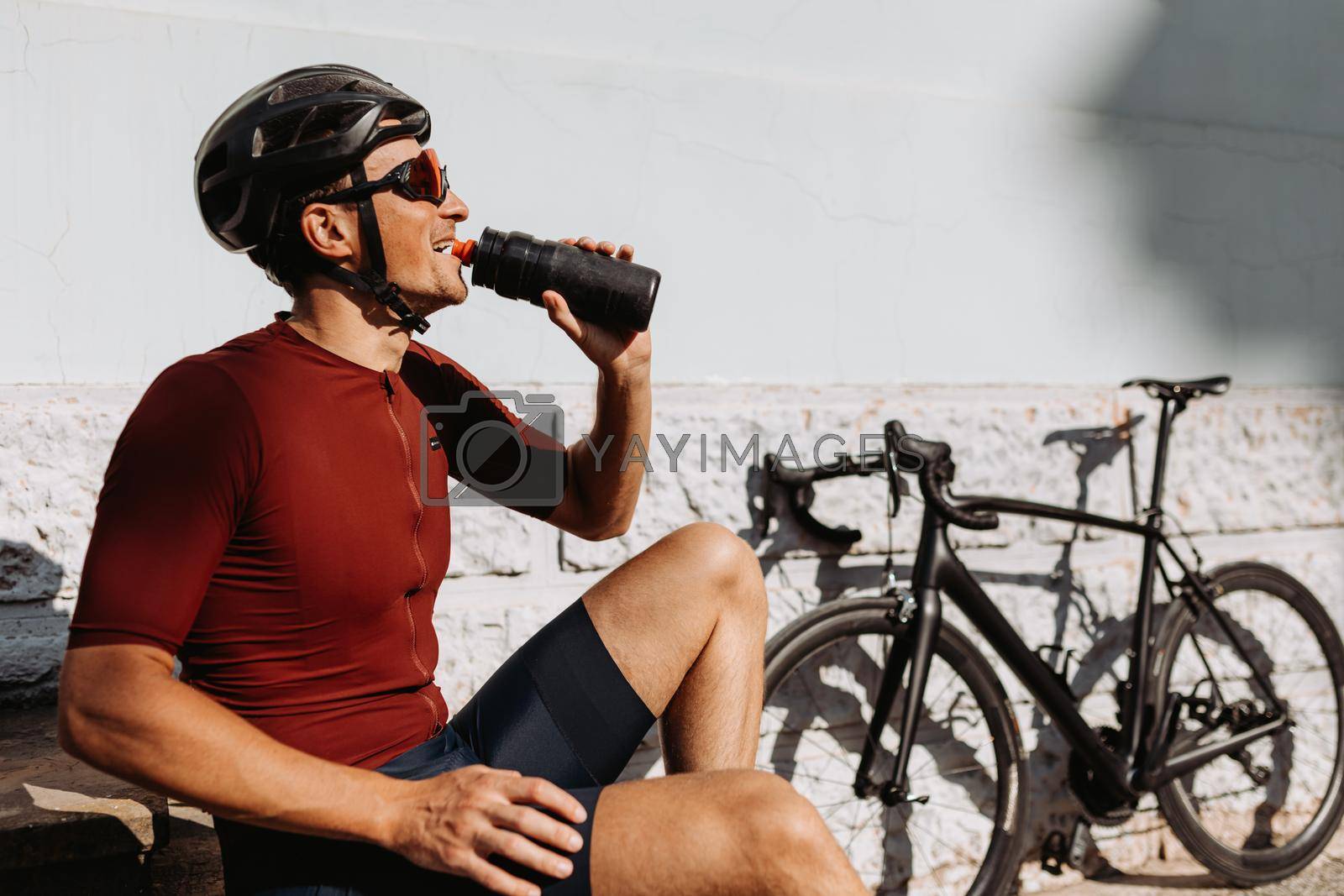 Royalty free image of Cyclist drinking water while sitting near bike outdoors by Tymoshchuk