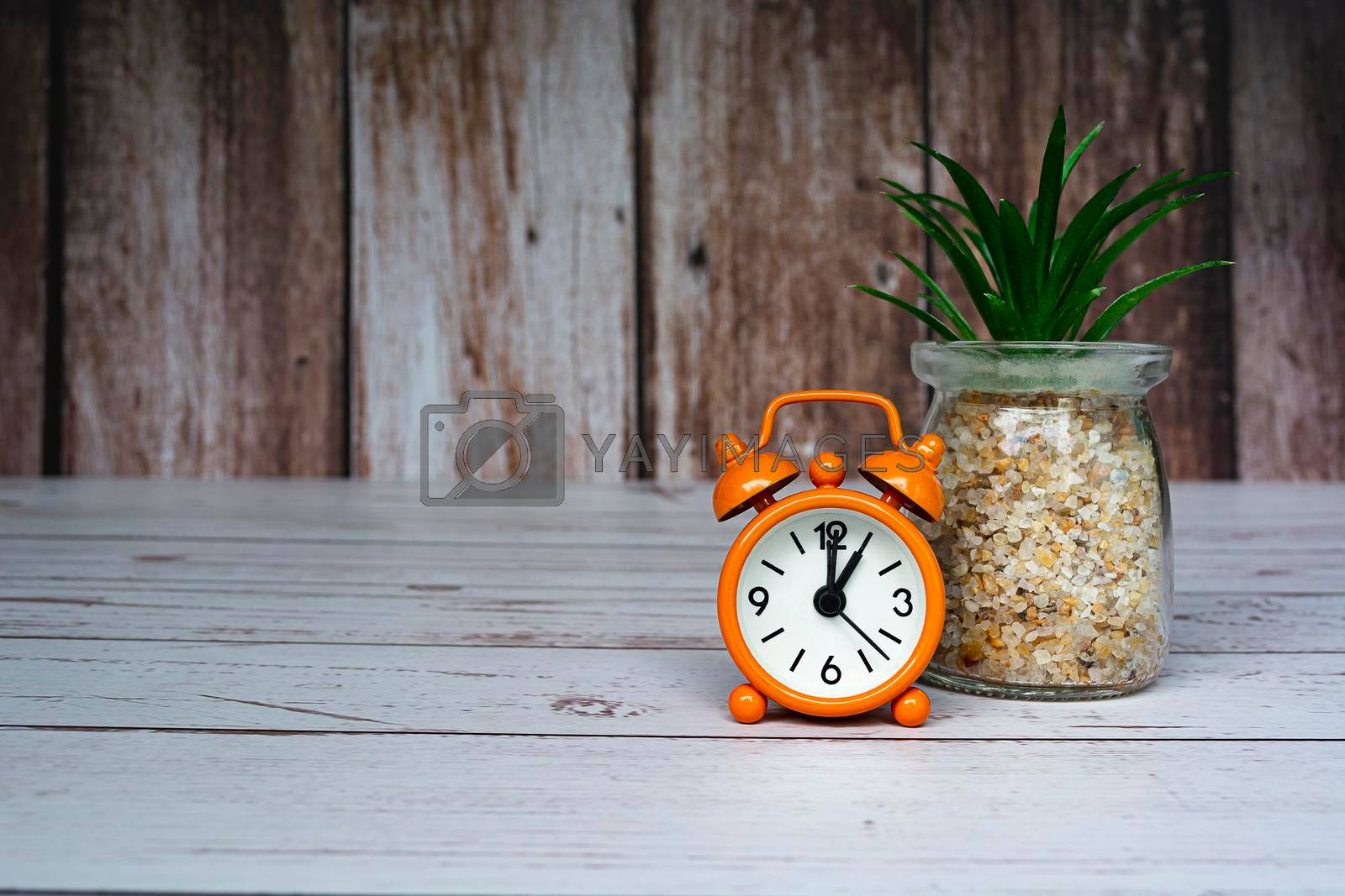 Royalty free image of Orange alarm clock isolated on wooden desk. The clock set at 1 o'clock. by JennMiranda