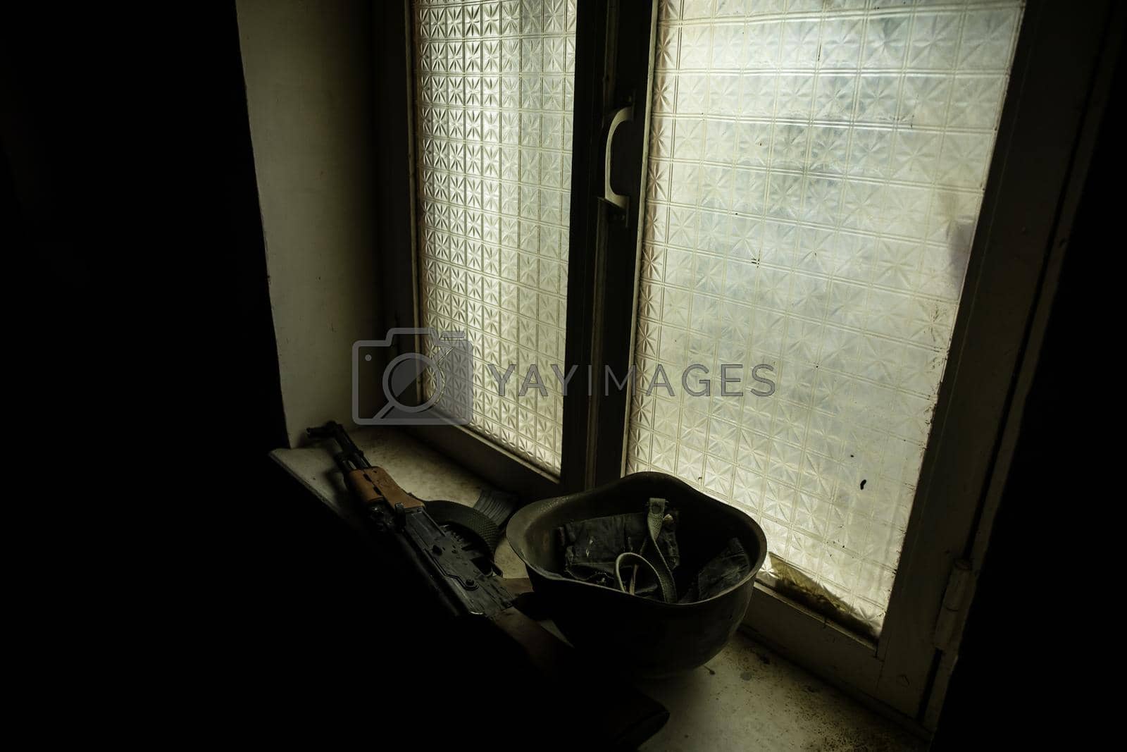 Conceptual photo of war between Russia and Ukraine. Russian weapon and helmet on windowsill at night. Old creepy room with window. Explosion outside.