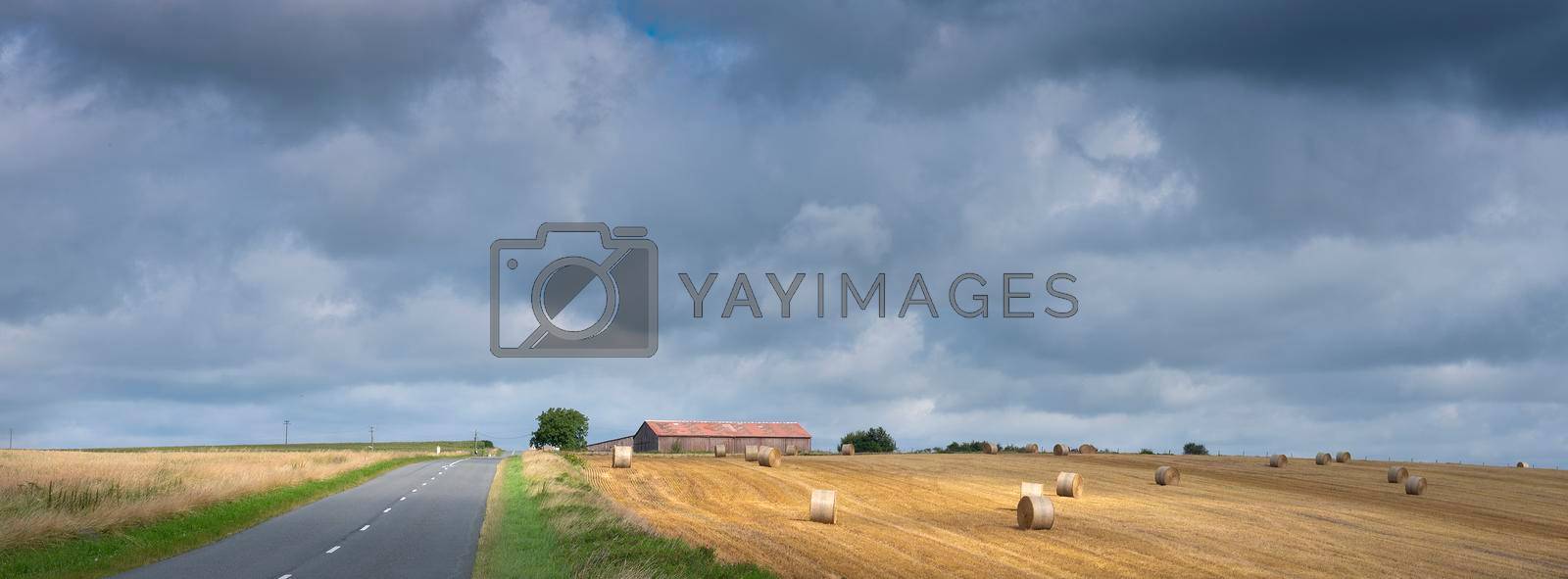 cloudy sky and summer countryside landscape with straw bales and barn in french ardennes near charleville