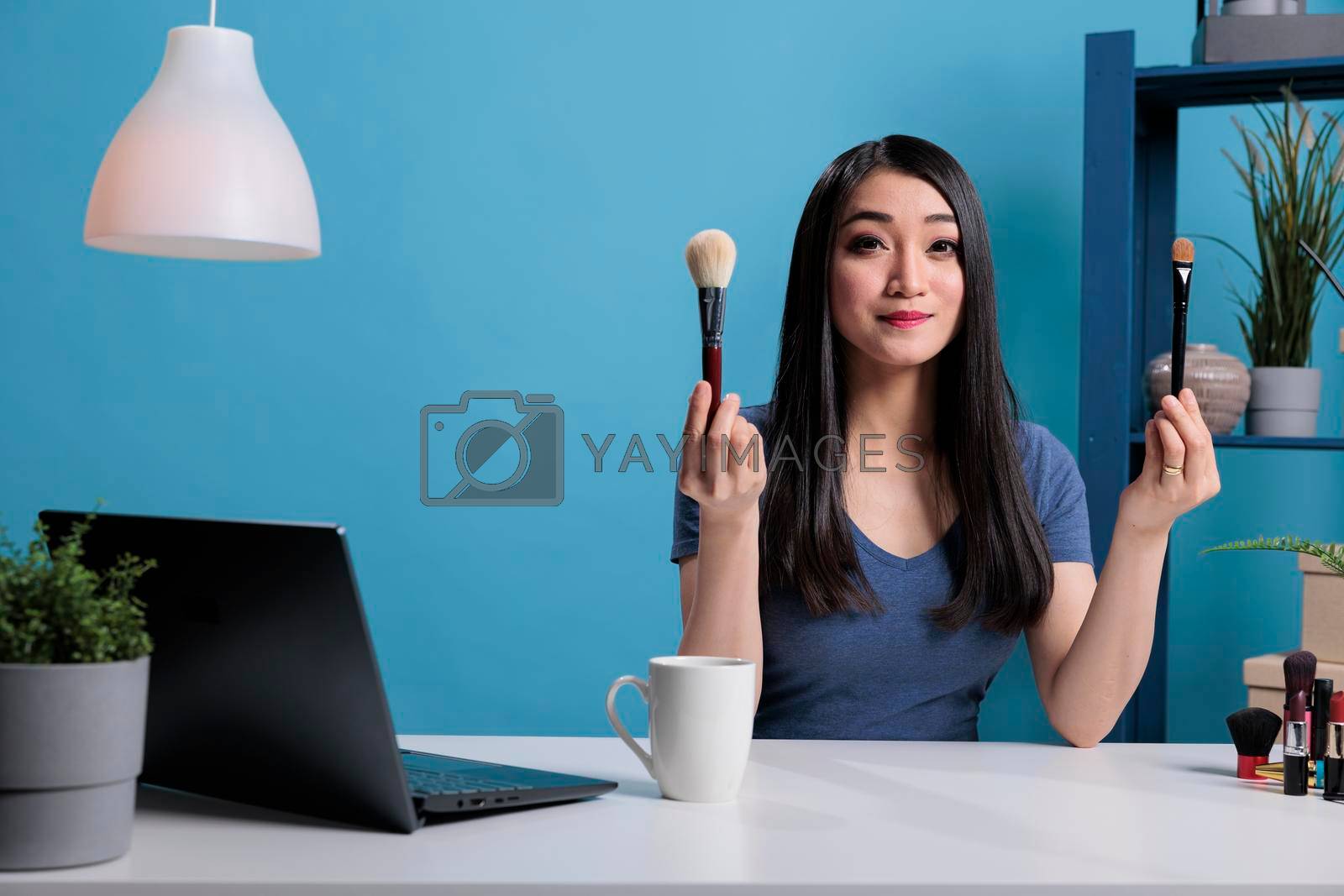 Beauty guru influencer holding make up brushes showing at camera while recording makeup tutorial for vlogging channel. Social media content creator advertising cosmetology products in studio