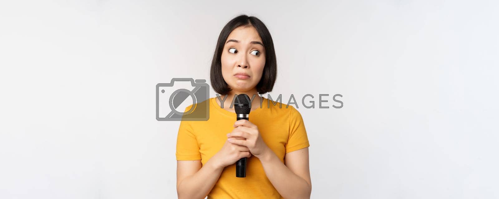 Royalty free image of Modest asian girl holding microphone, scared talking in public, standing against white background by Benzoix