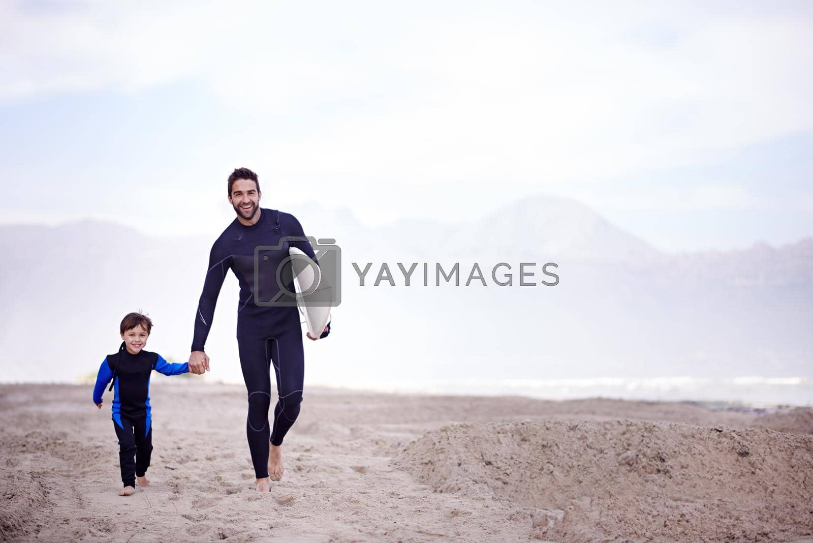 A father walking along the beach with his young son before a surfing lesson.