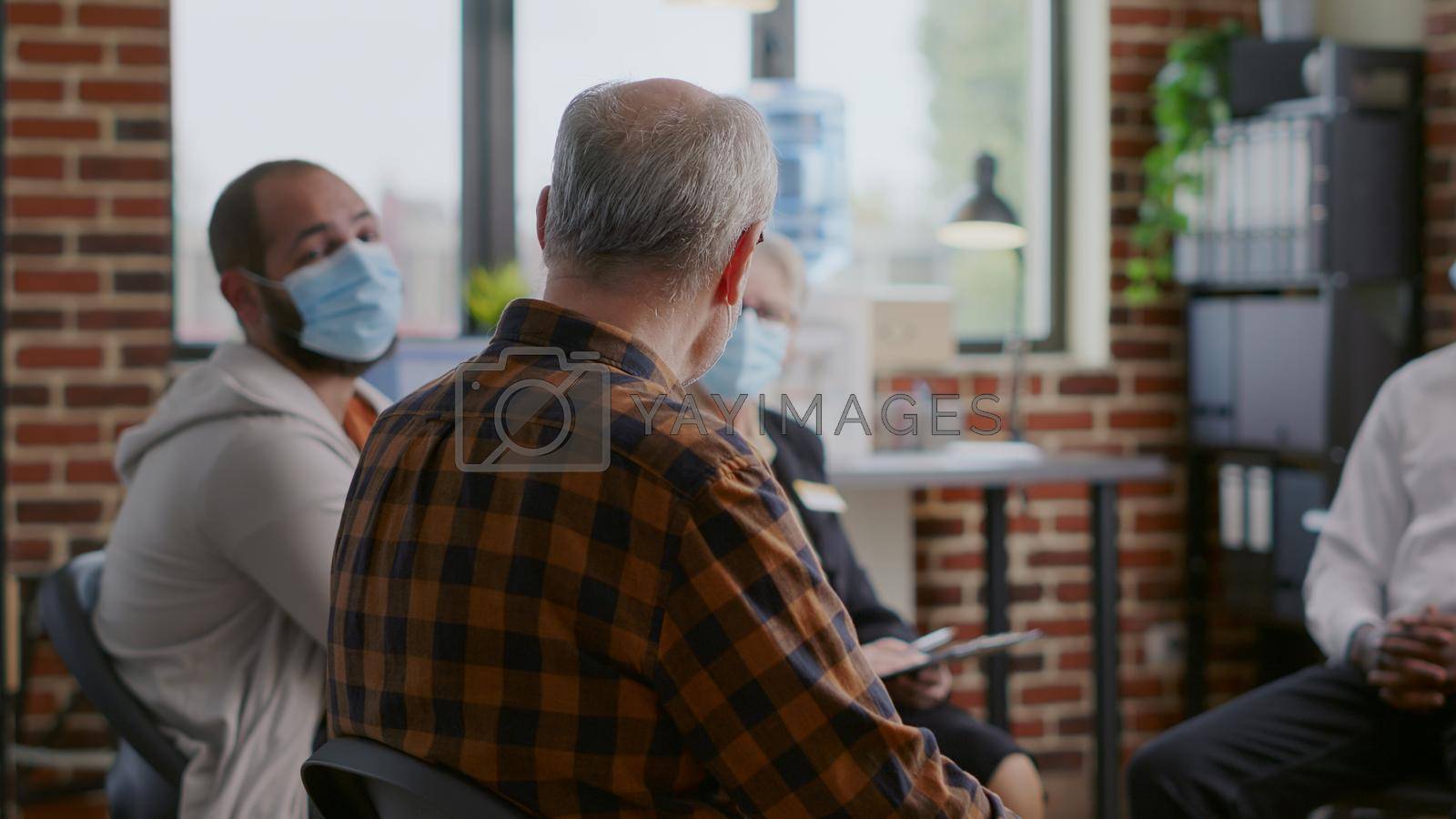Close up of senior man attending aa group therapy meeting with people. Person wearing face mask and having conversation with patients about alcohol addiction at rehabilitation program.