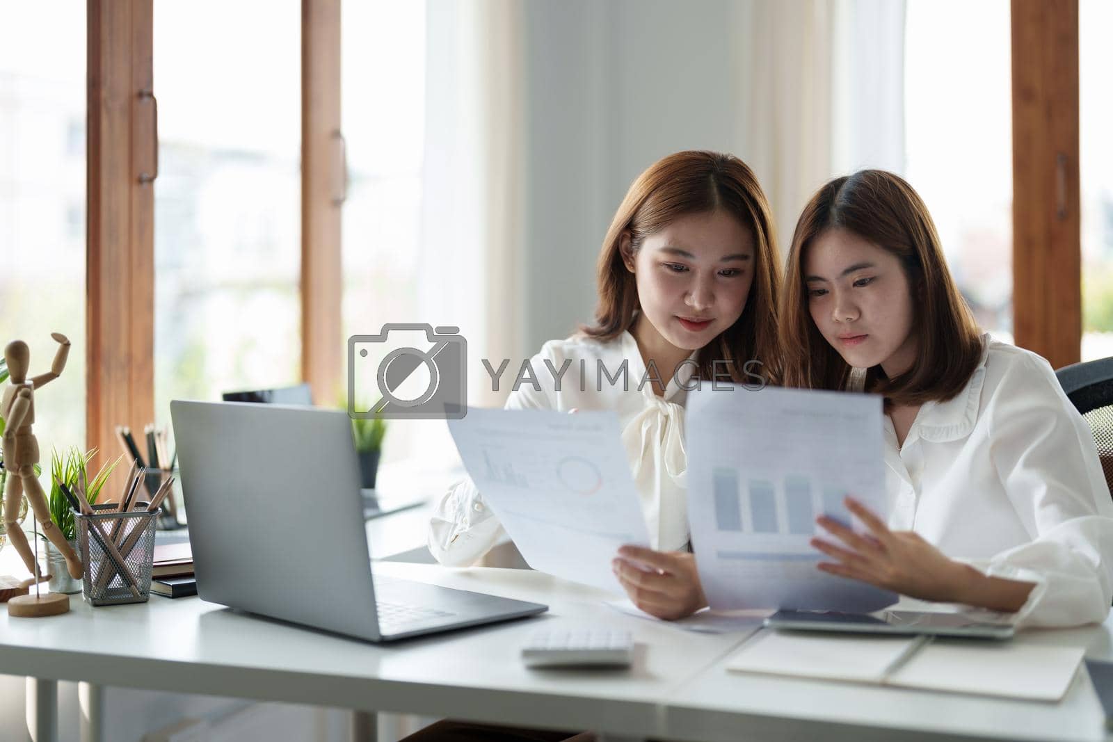 Two colleagues or students, asian girl are using a laptop while sitting at workplace discussing about job or education.