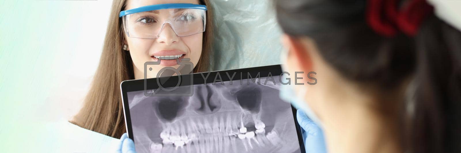 Portrait of cheerful female at dentist appointment. Stomatologist holding dental panoramic X-ray in hands. Dental care, stomatology clinic and healthy teeth concept