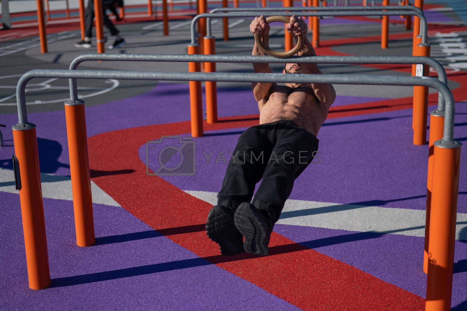 Royalty free image of Shirtless man doing horizontal balance on parallel bars at sports ground. by mrwed54