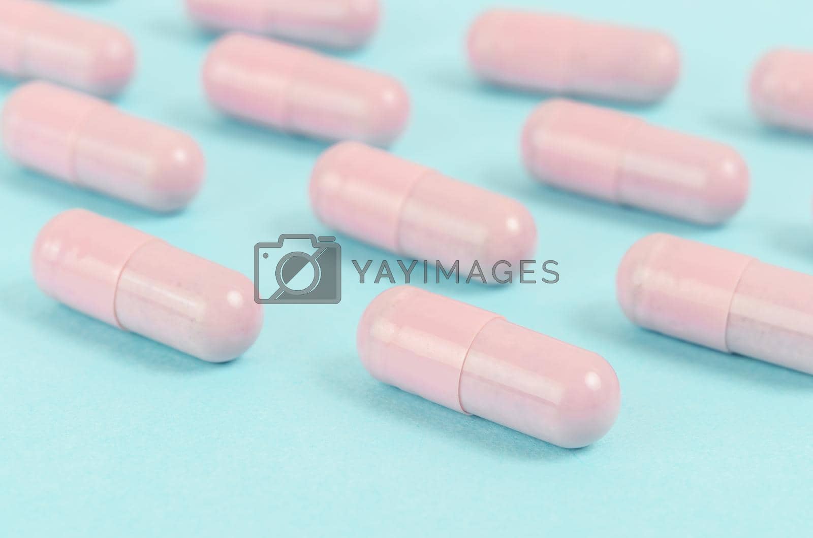 Royalty free image of Pink capsule pills on blue background. by Gamjai