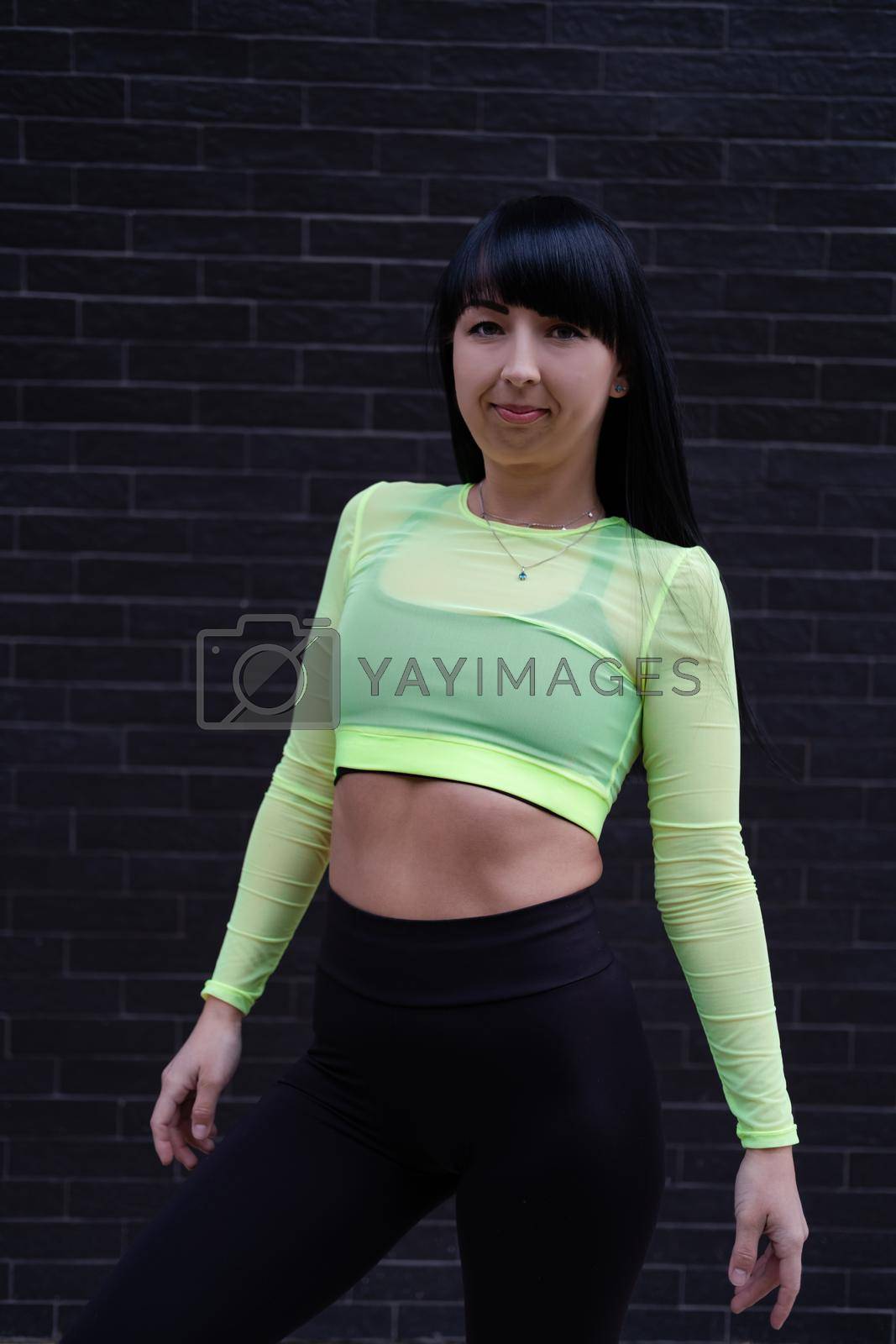 charming fitness sport girl in fashion trendy black and green sportswear on background on black brick wall.