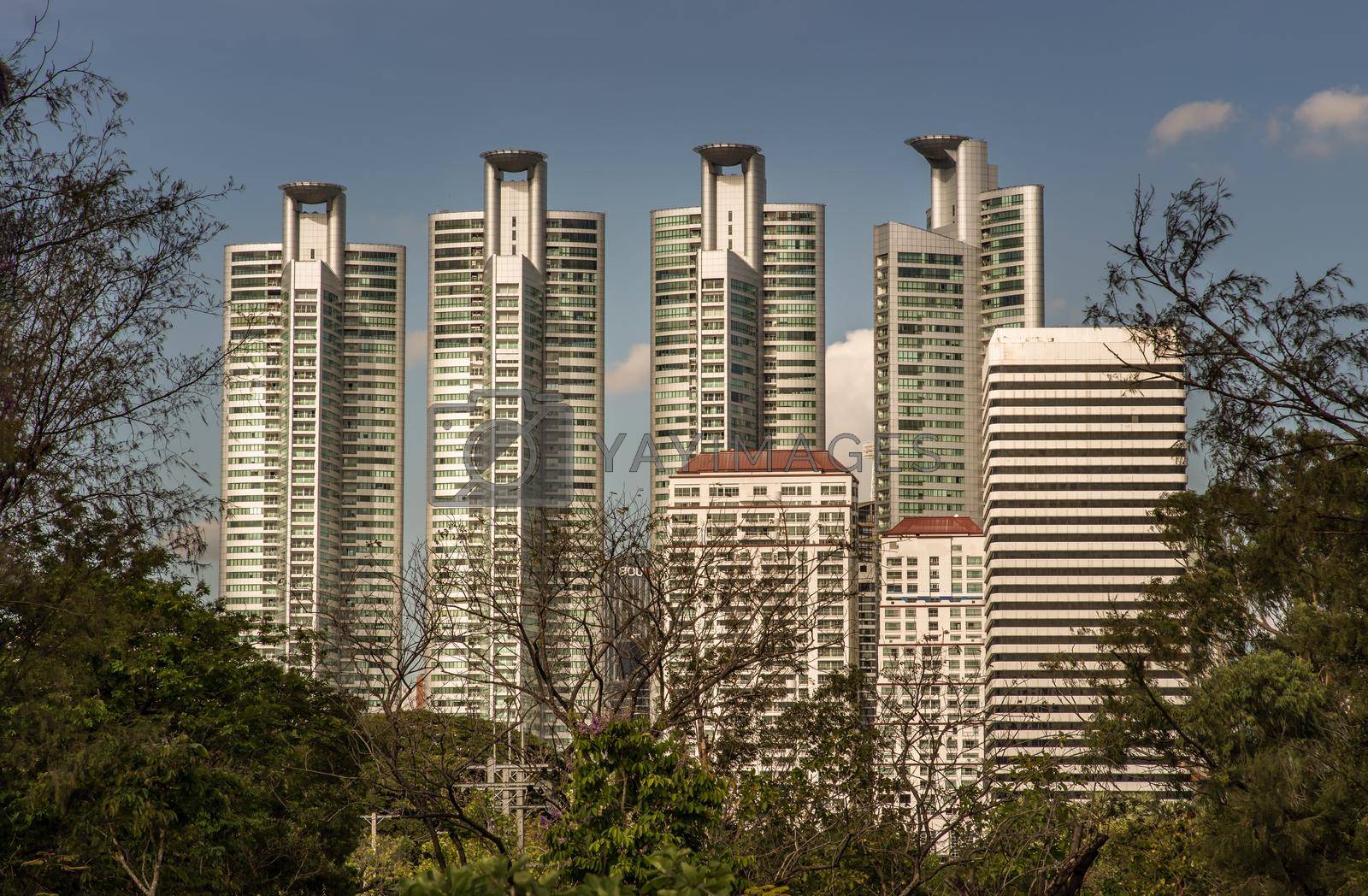 Bangkok, Thailand - Feb 19, 2022 : View of Modern high buildings among green trees space in nature against blue sky with clouds at afternoon. City growth concept, Selective focus.