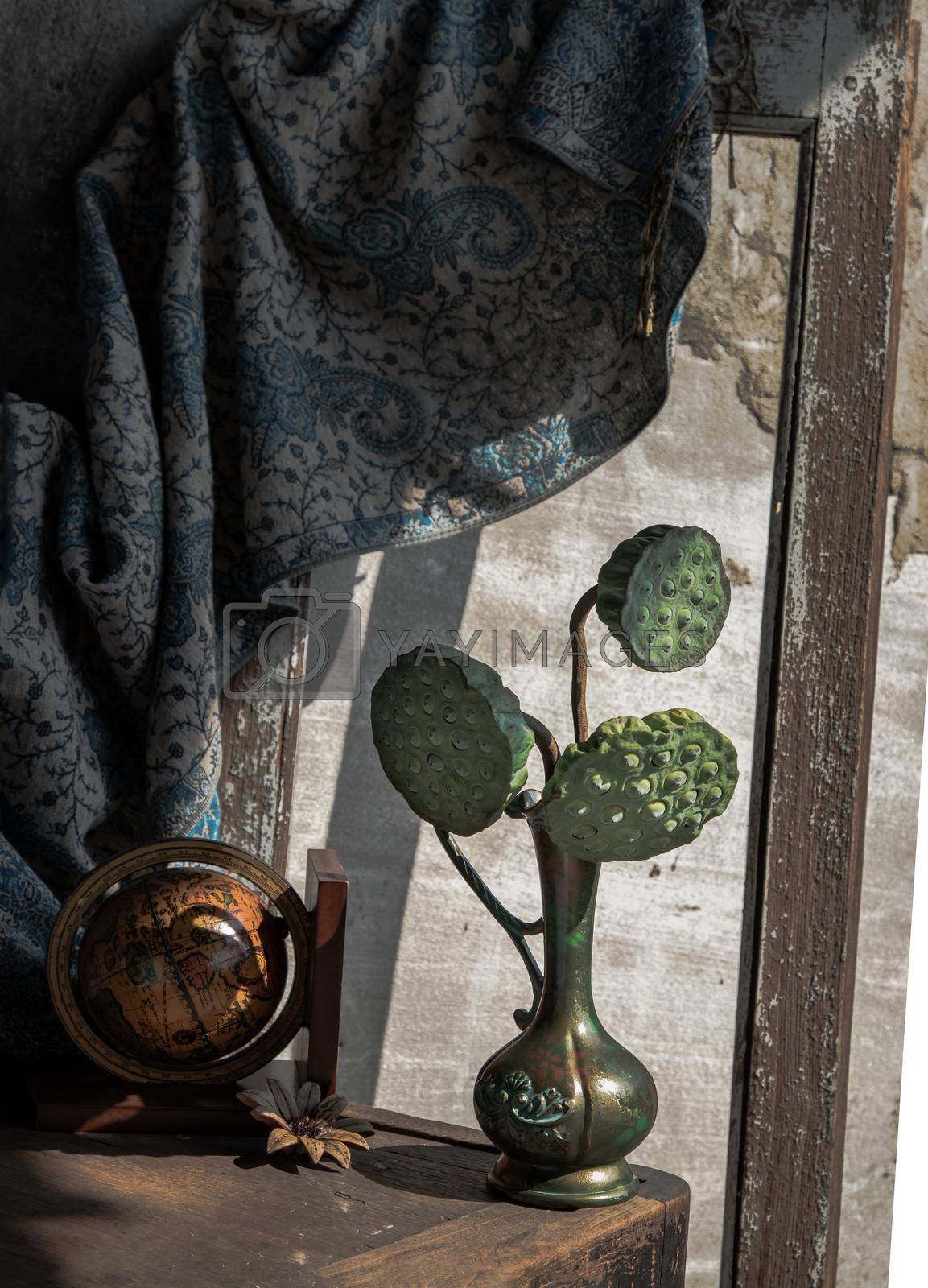 Fresh green lotus seed pods in Antique carved iron jug or vase with Wood globe on Old wooden chair. Dark tone, Selective focus.