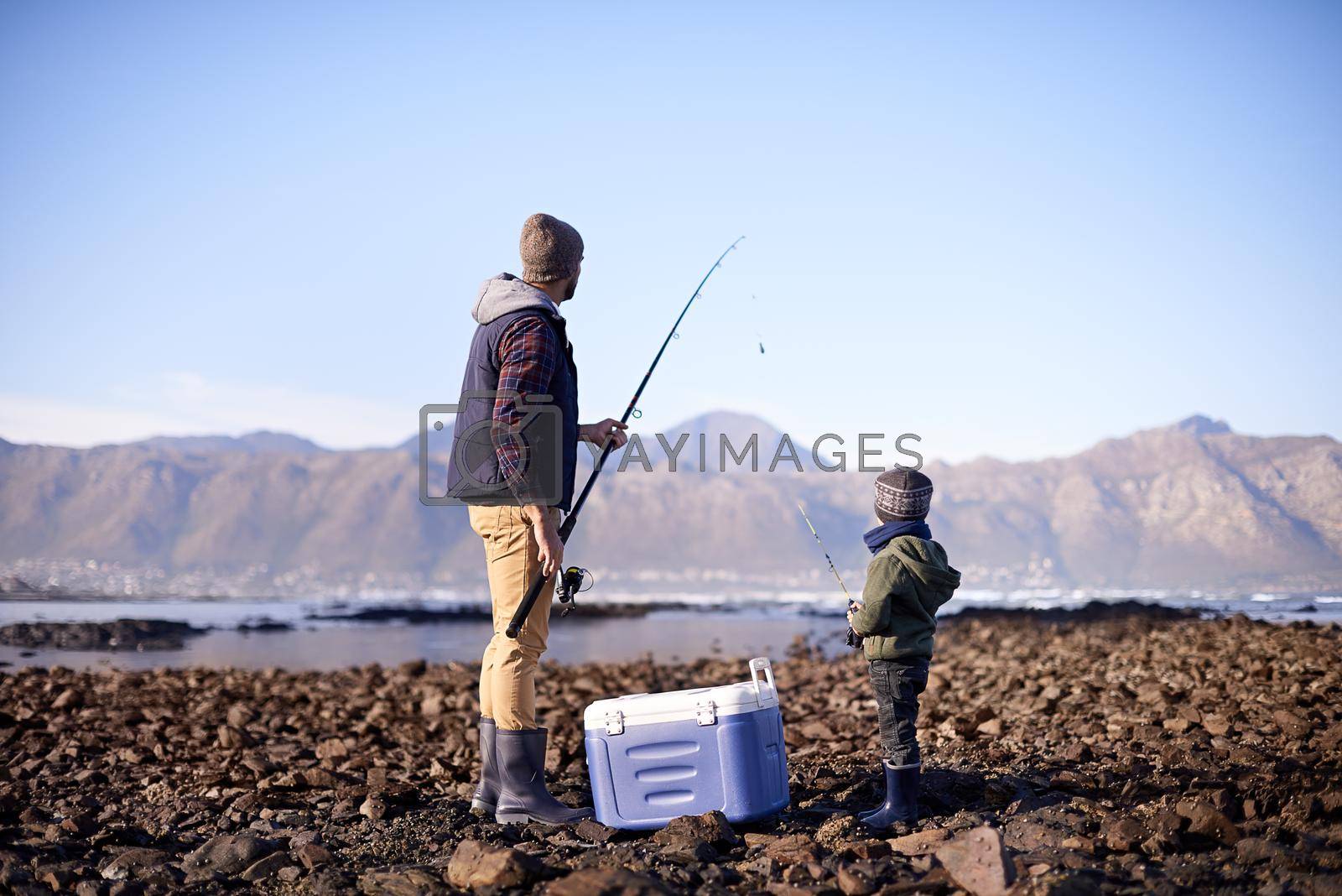Shot of a father and son standing with their fishing gear by the sea.