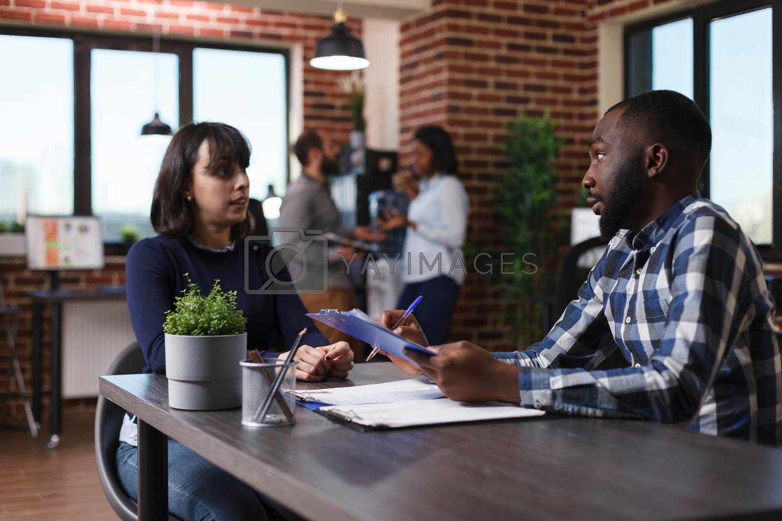 Business company employer asking woman questions about her work experience in field. African american recruiter reviewing young adult candidate CV while talking about career opportunity.