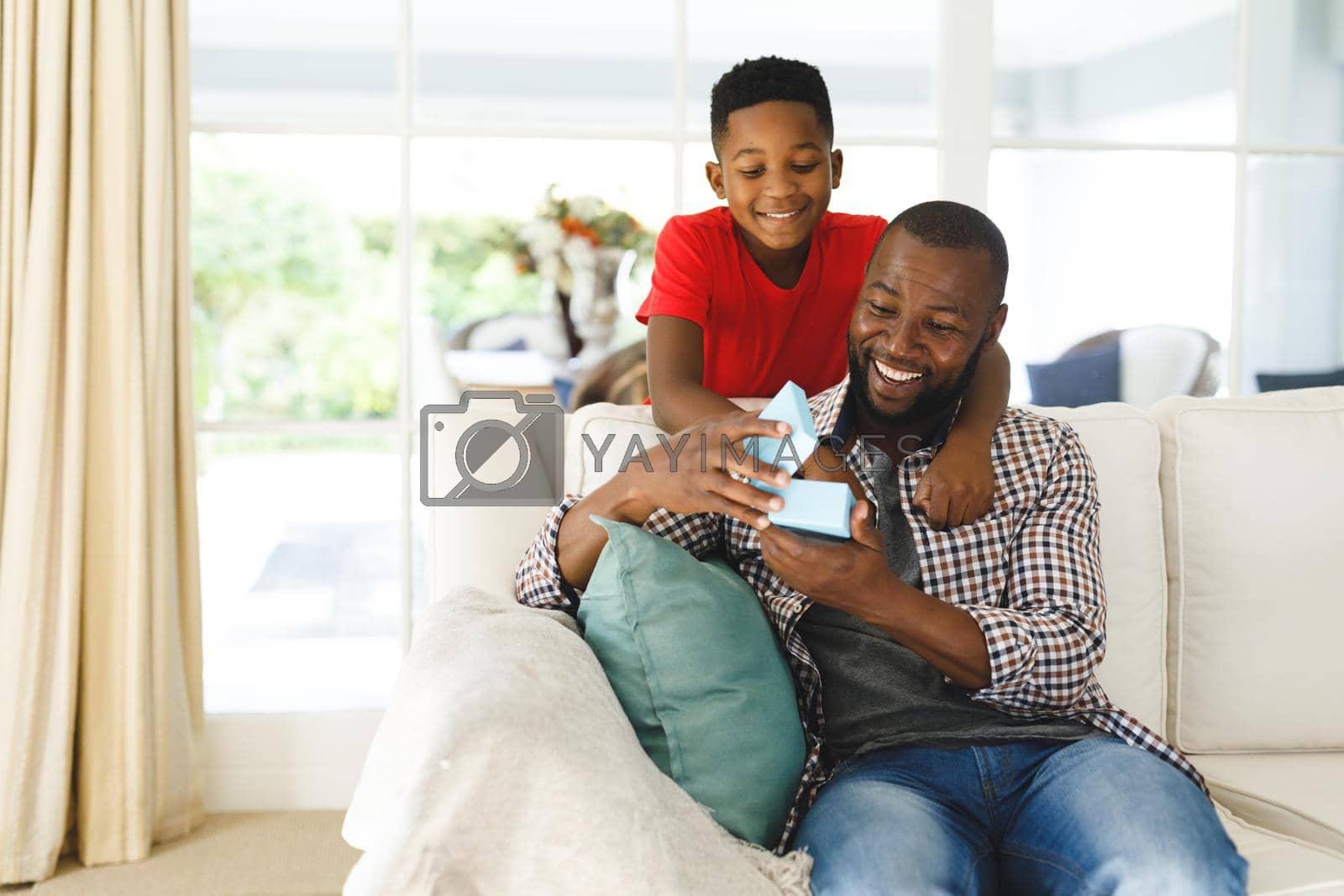 Royalty free image of African american father opening gift from his son and smiling in living room by Wavebreakmedia