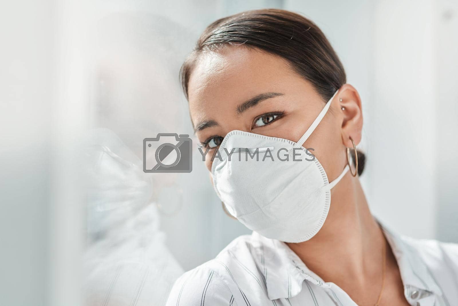 Royalty free image of 2020 The year of the face mask. Shot of a masked young businesswoman leaning against a window in a modern office. by YuriArcurs