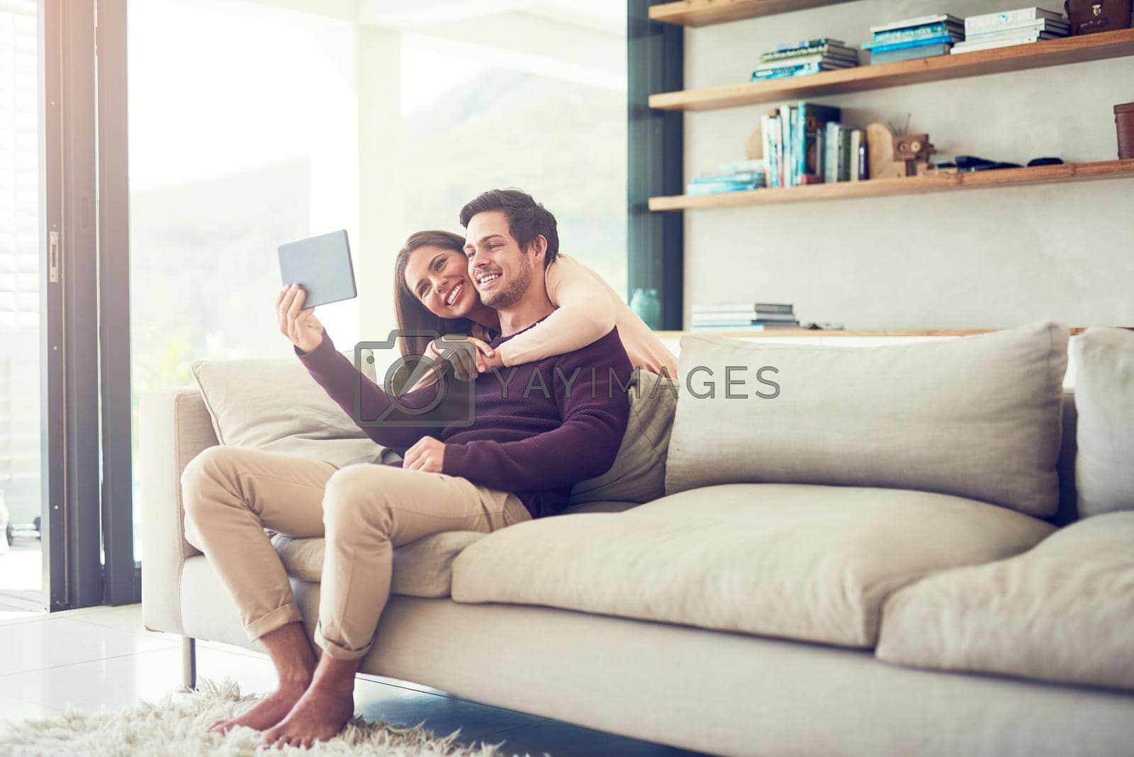 Shot of a smiling young couple using a digital tablet while relaxing on the sofa at home.