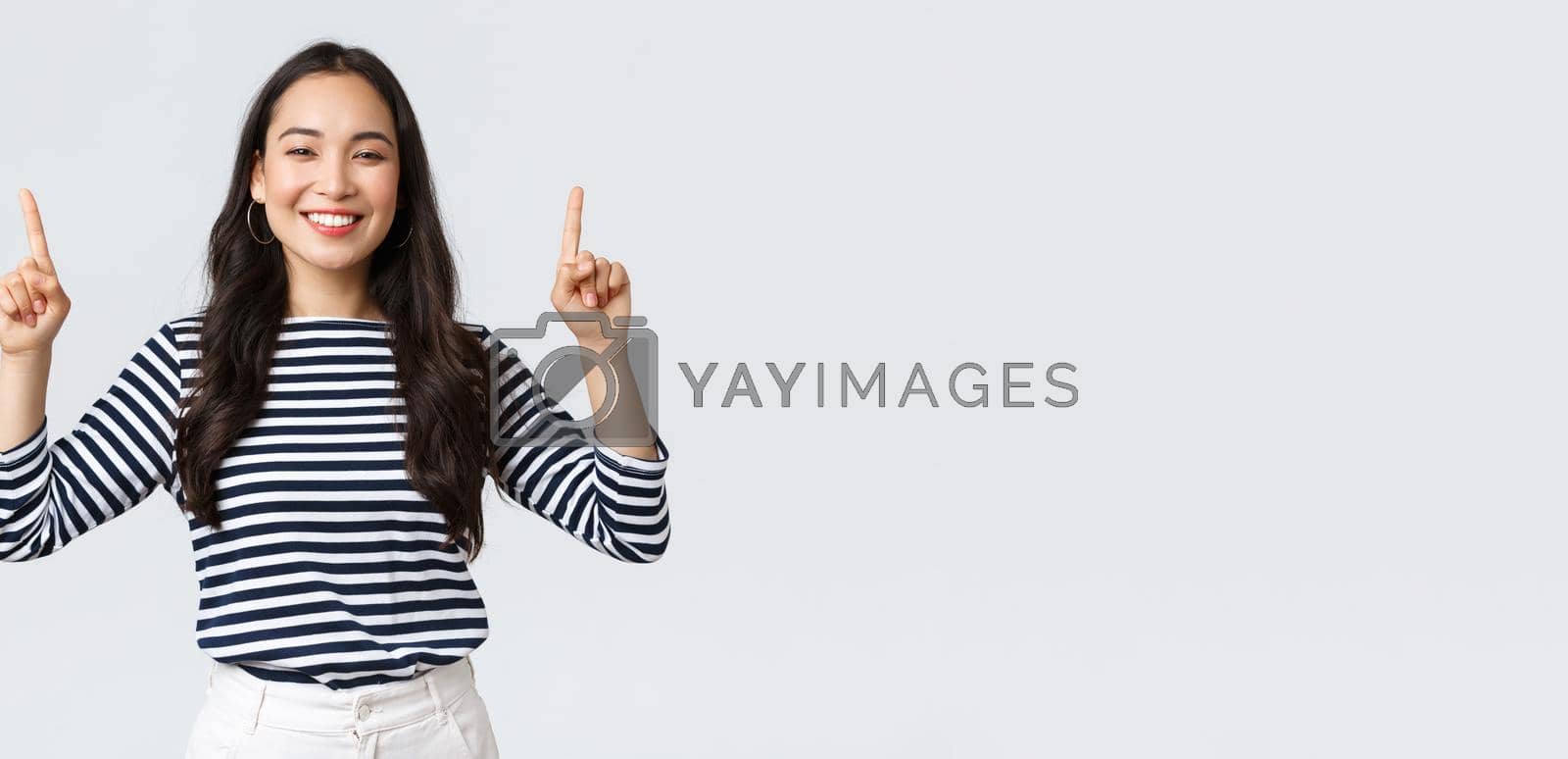 Lifestyle, beauty and fashion, people emotions concept. Cheerful good-looking female model pointing fingers up to shop promotion banner, smiling camera, recommend click link to online store.