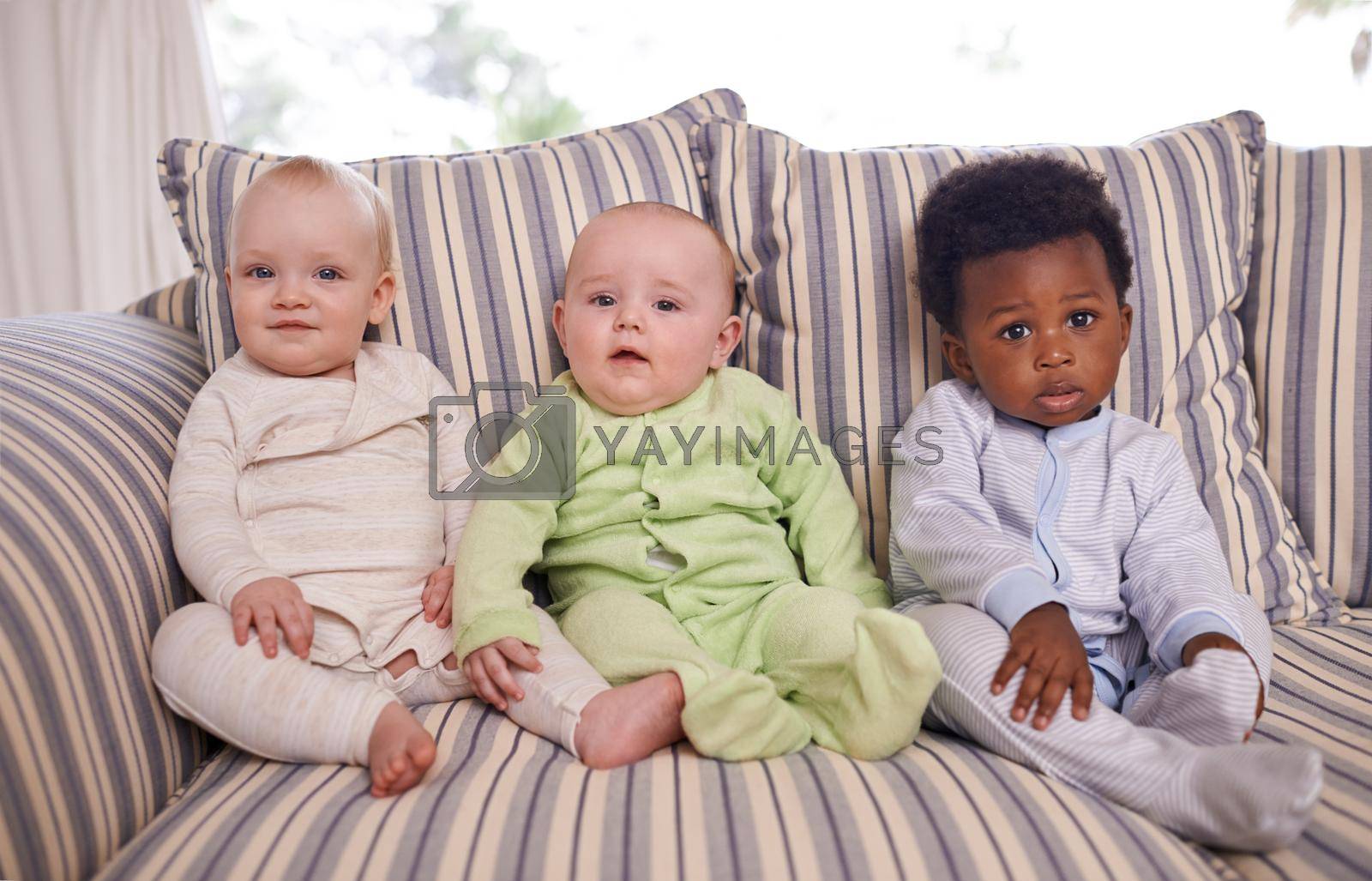 Portrait of three adorable babies sitting on a couch.