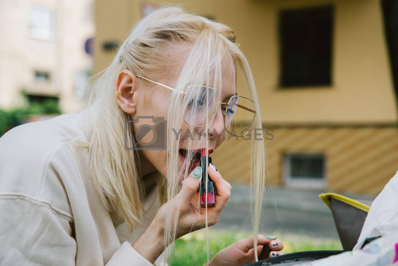 Royalty free image of young smiling hipster happy woman doing make-up using lipstick and mirror outdoors by Ashtray25