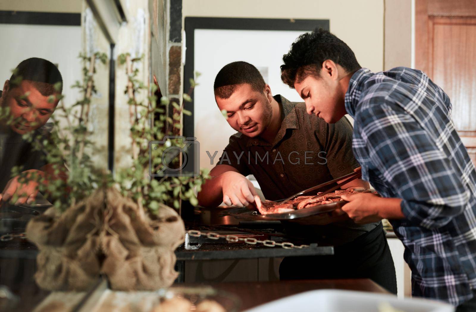 Shot of two young men grilling meat while having a barbecue.
