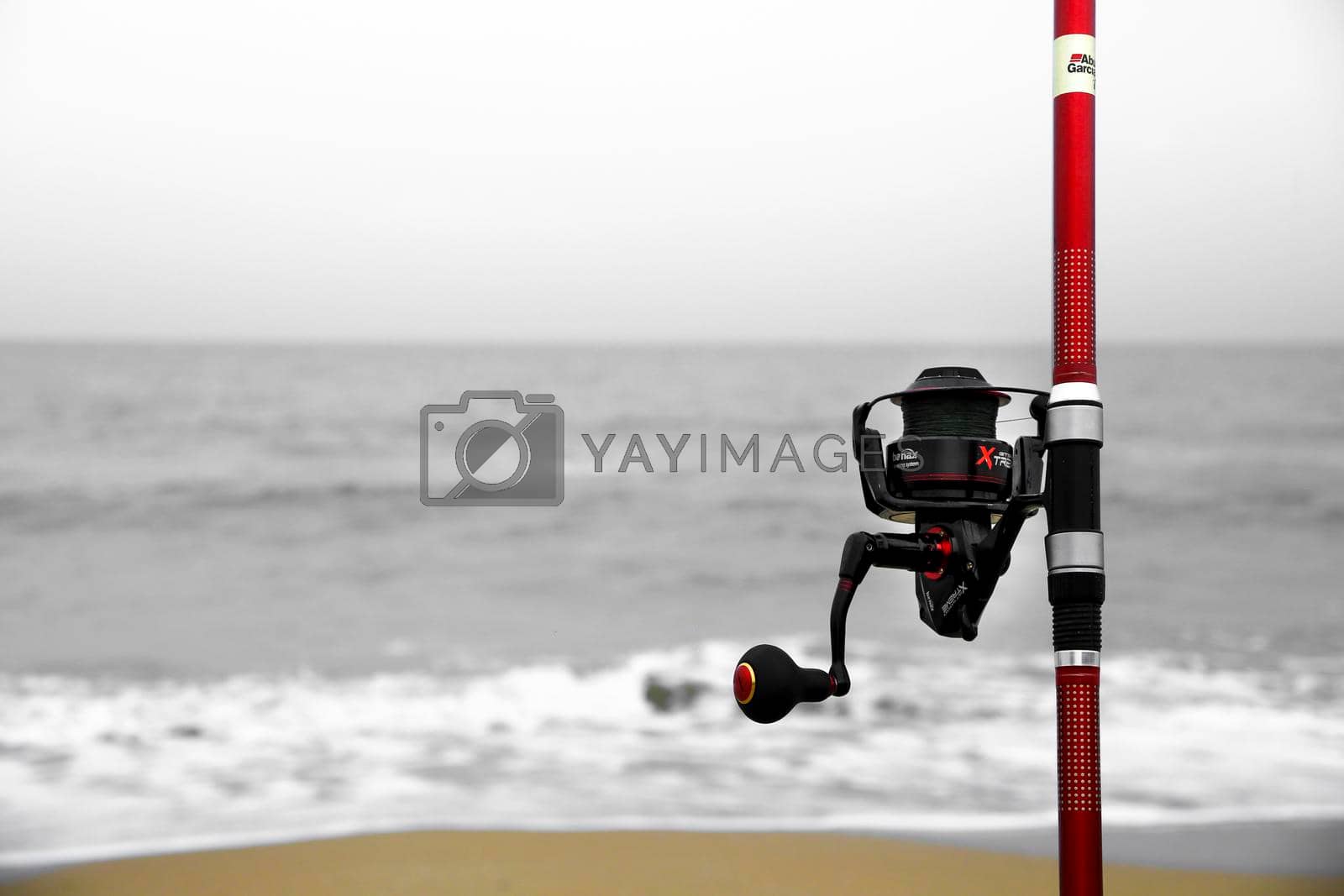 El Pinet, Alicante, Spain- March 30, 2022: Red Fishing rod on the shore on a cloudy day on El Pinet Beach in Alicante