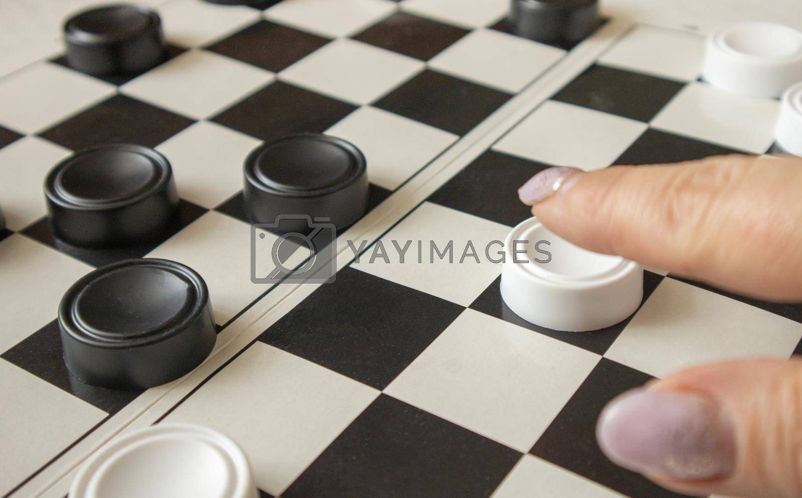 A woman's hand moves a white checker on a black-and-white playing field, the concept of hobbies and home games.