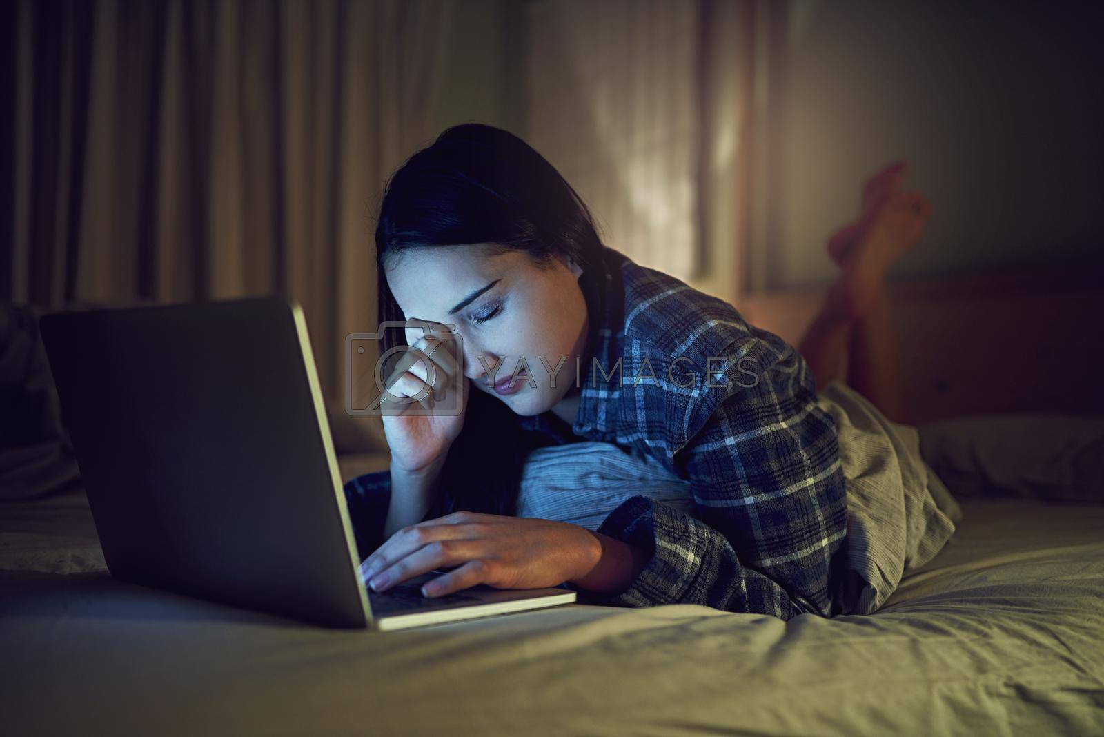 Royalty free image of Its been a late night online. Shot of a sleepy young woman using a laptop late at night while lying on her bed in her bedroom. by YuriArcurs
