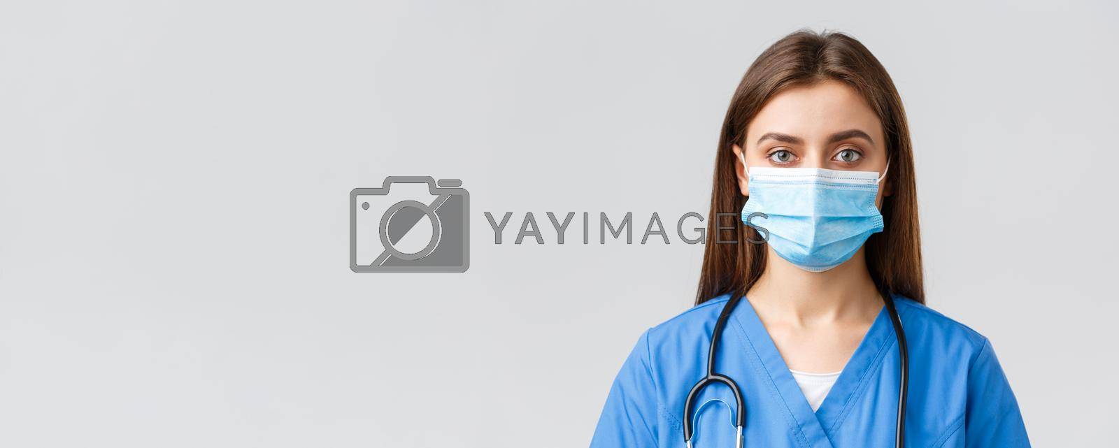 Covid-19, preventing virus, health, healthcare workers and quarantine concept. Close-up young female nurse or doctor in blue scrubs and medical mask looking serious at camera.