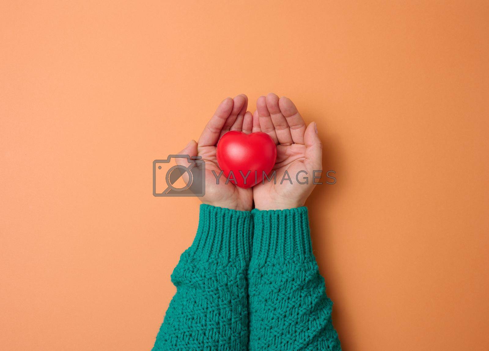 female hands holds red heart, orange background. Love and donation concept