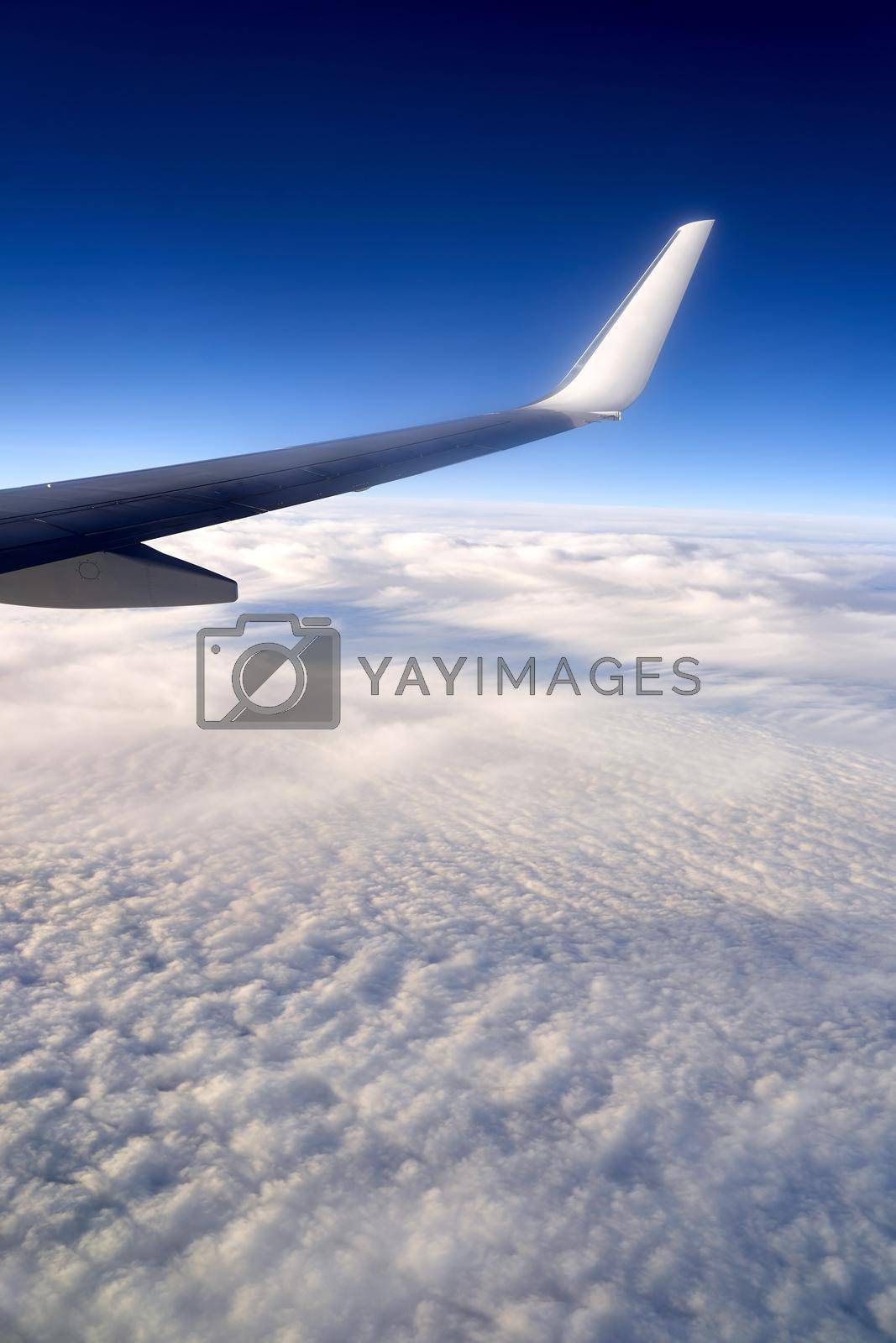 View of airplane wing on blue sky background. Plane over clouds in the sky.