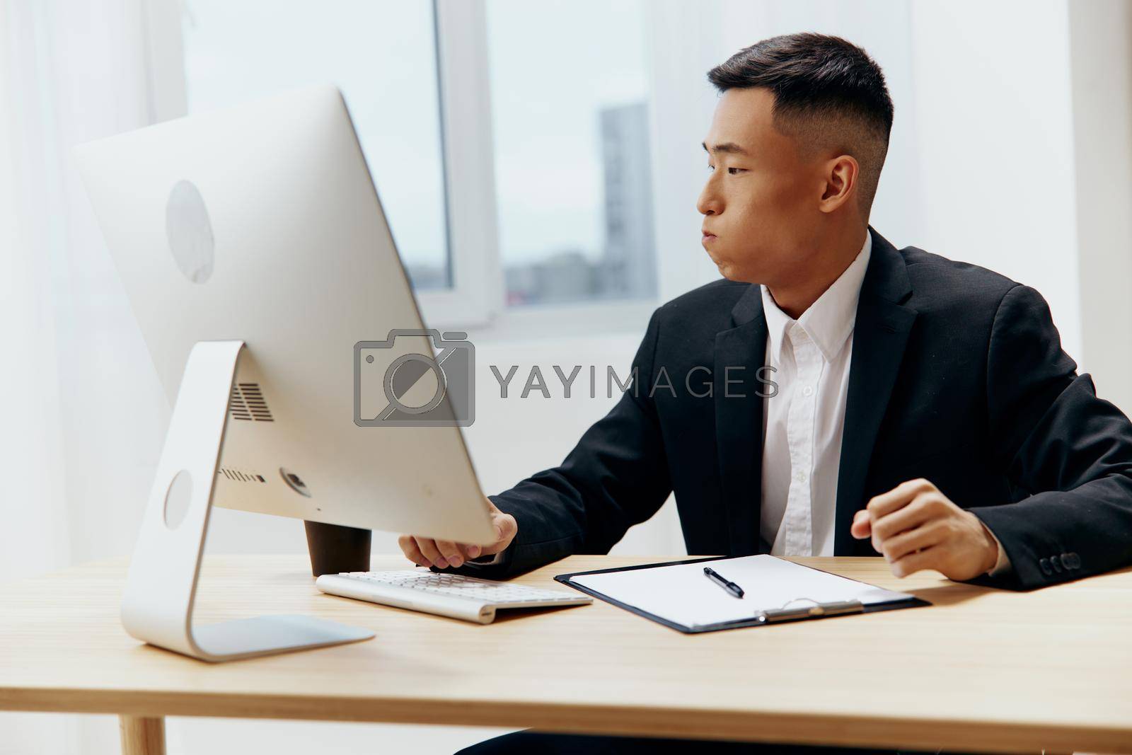Asian man sitting at a desk in front of a computer Lifestyle. High quality photo